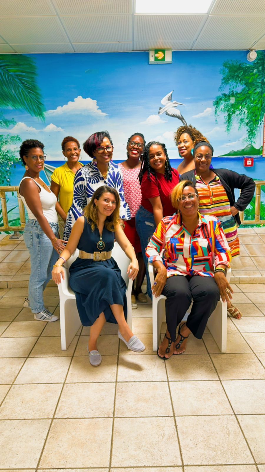 A group sits casually along a wall with bright tropical beach murals in a tiled hallway.