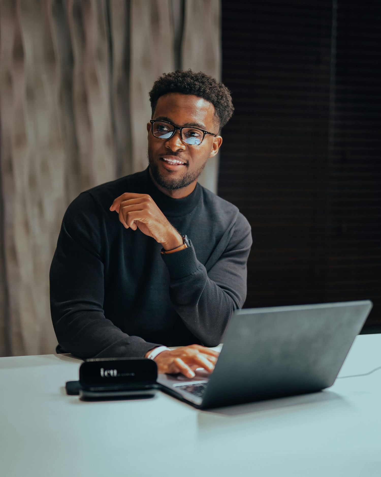 Professional freelancer working at desk with laptop and glasses in dark office setting.