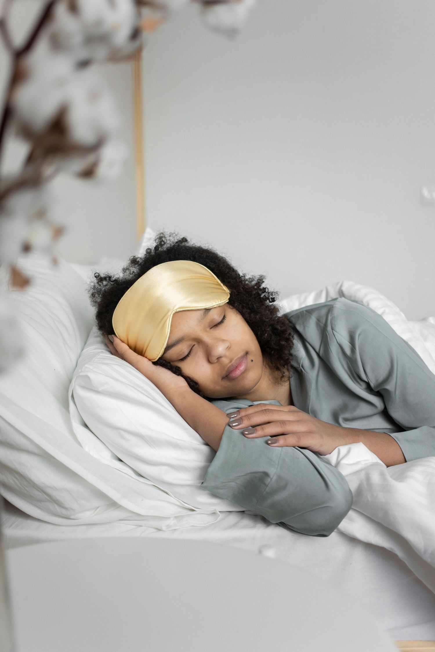 Someone sleeping peacefully in bed wearing a grey sweater against white bedding and pillows.