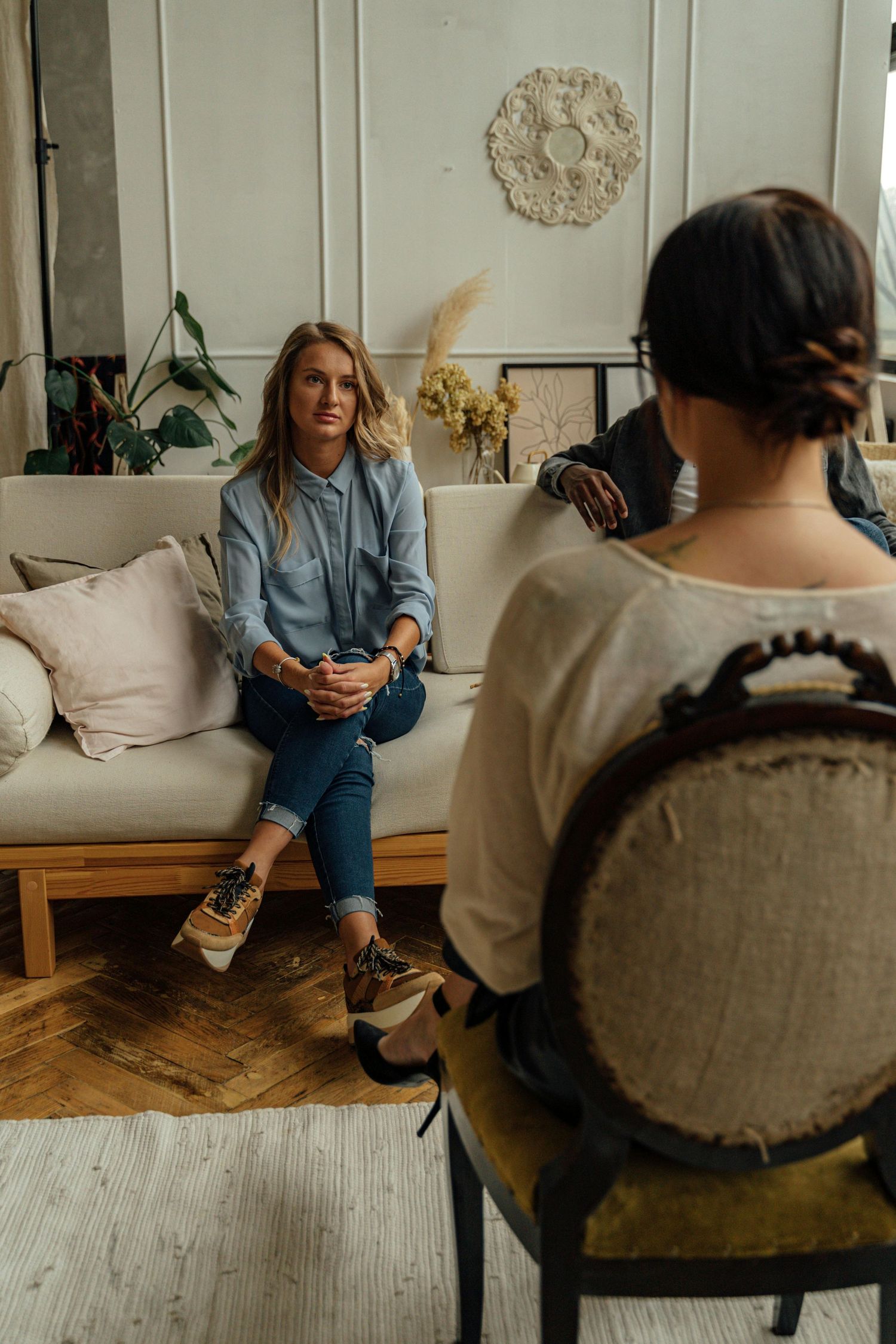 Person in denim sits on beige sofa having a thoughtful conversation in modern living room with hardwood floors.