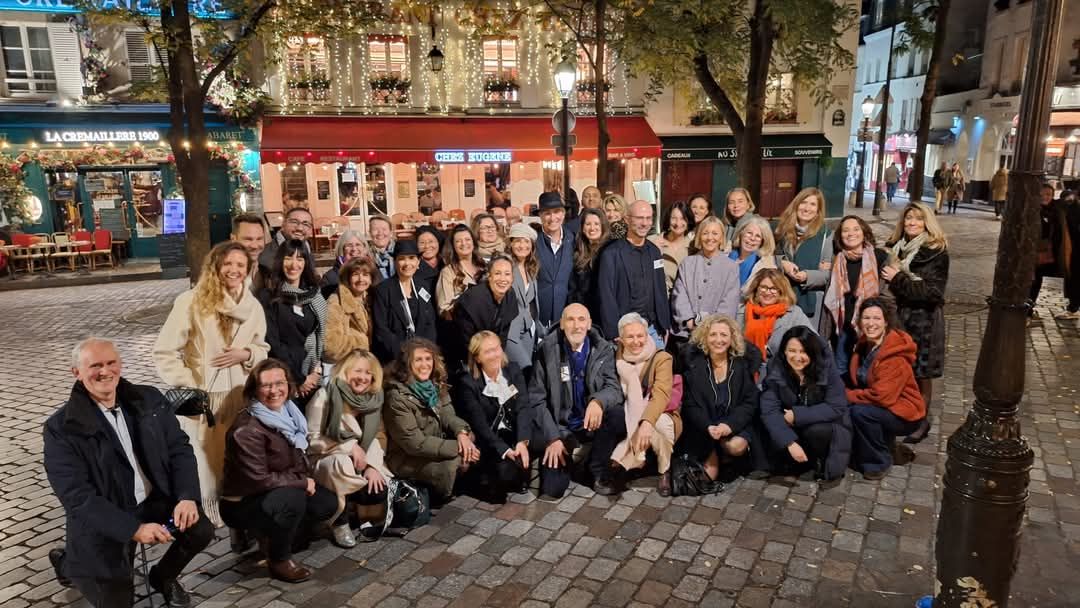 Large group of people sitting outdoors in a row at a social gathering event on a cobblestone walkway.