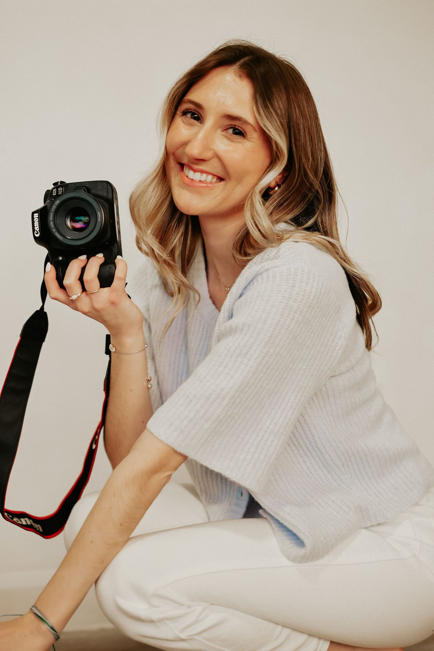 Close-up portraits of a photographer in white holding a professional camera against light background.