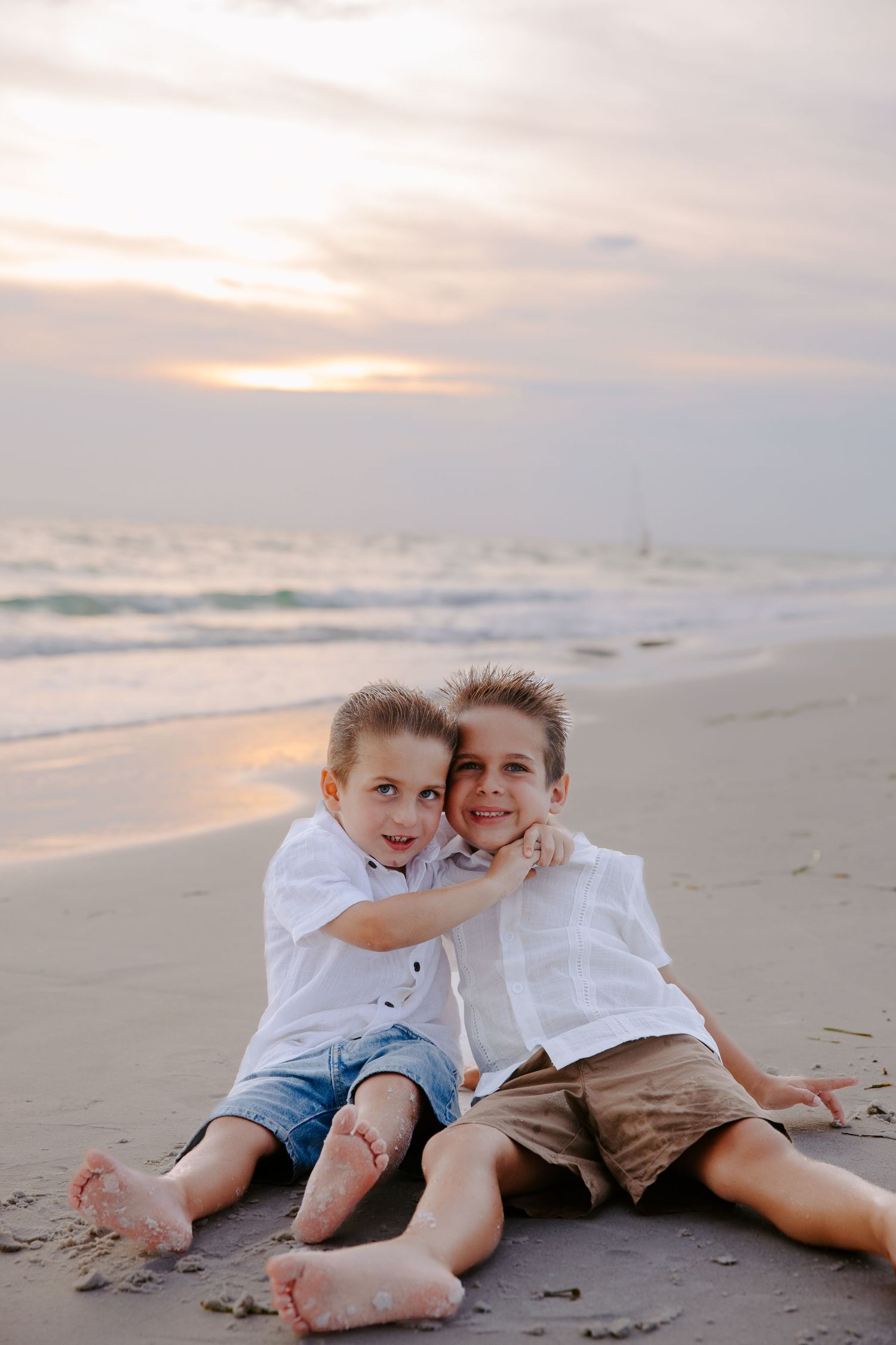 Two children relaxing together on sandy beach at sunset.