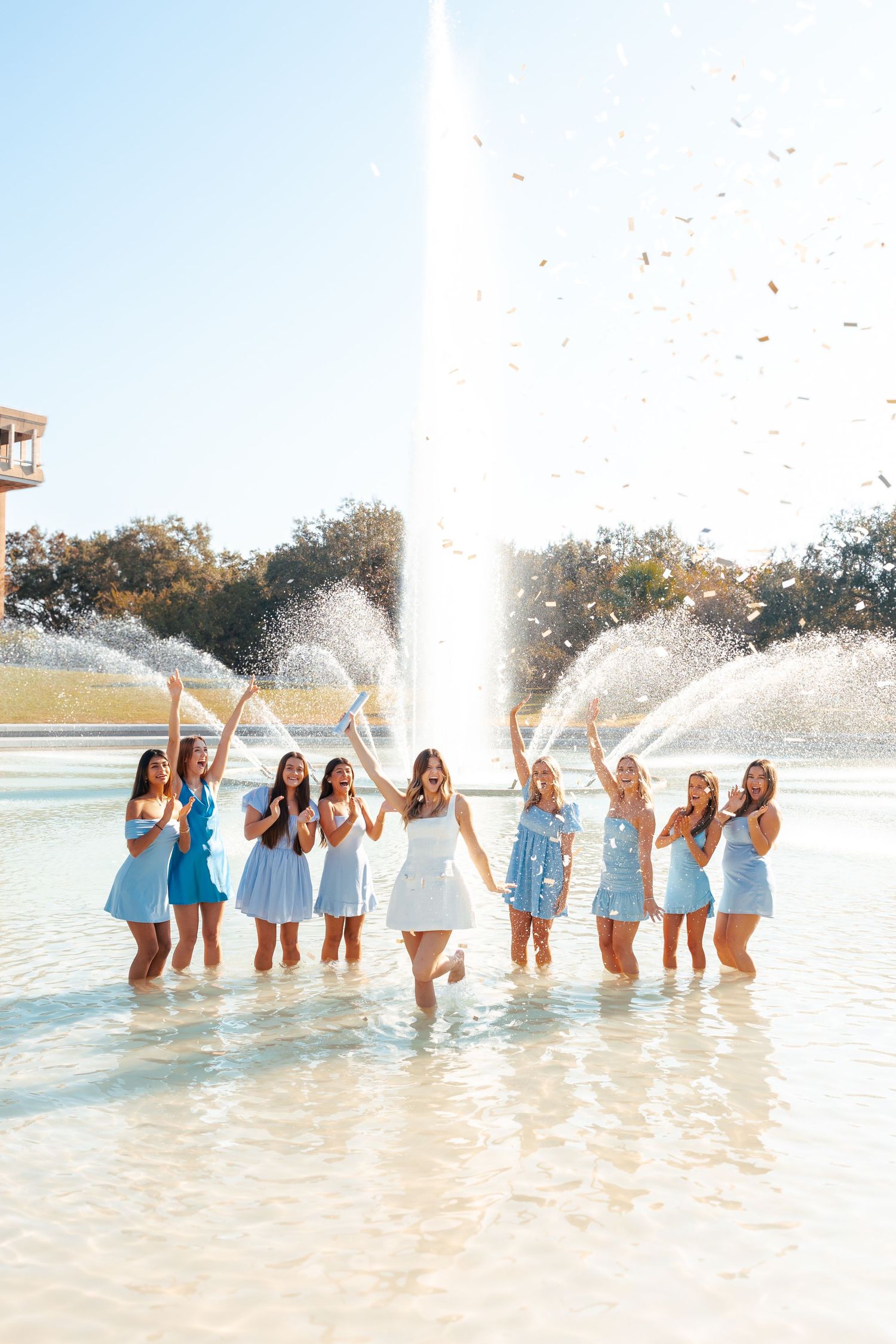 A group of friends splash and play in shallow water wearing white and blue outfits during a summer photoshoot.