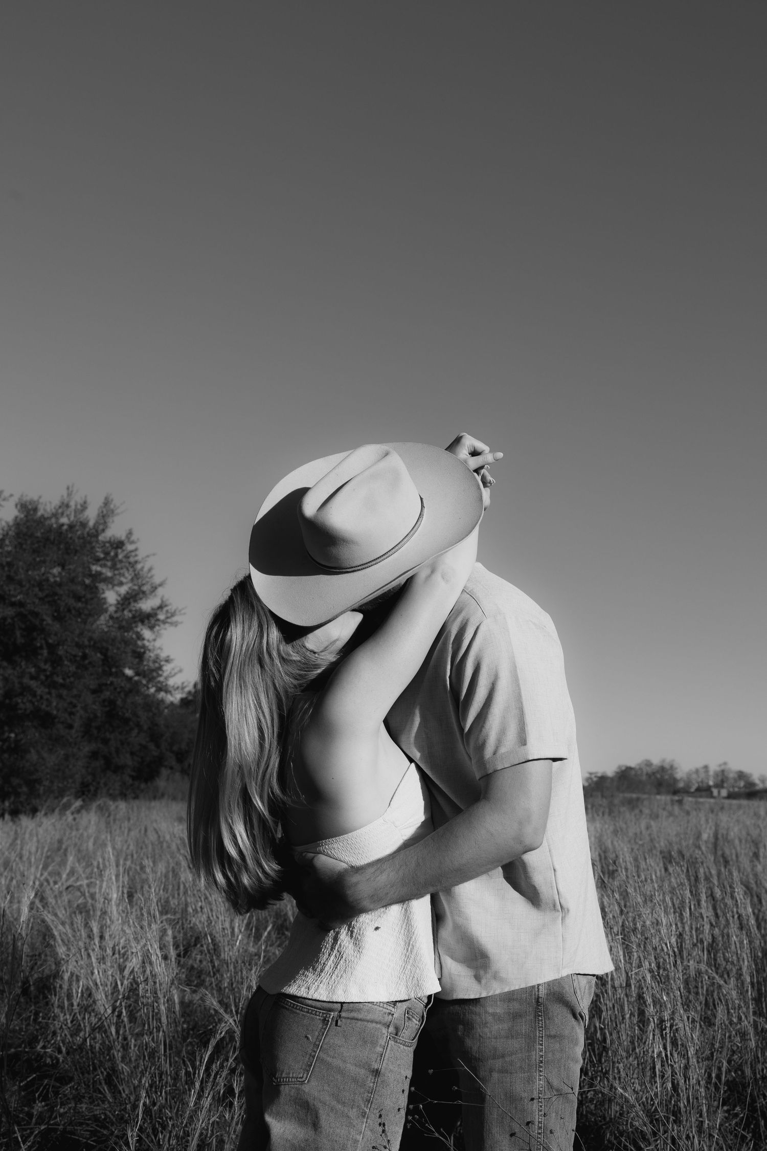 Black and white photo series showing two people embracing in a grassy field against a cloudy sky.