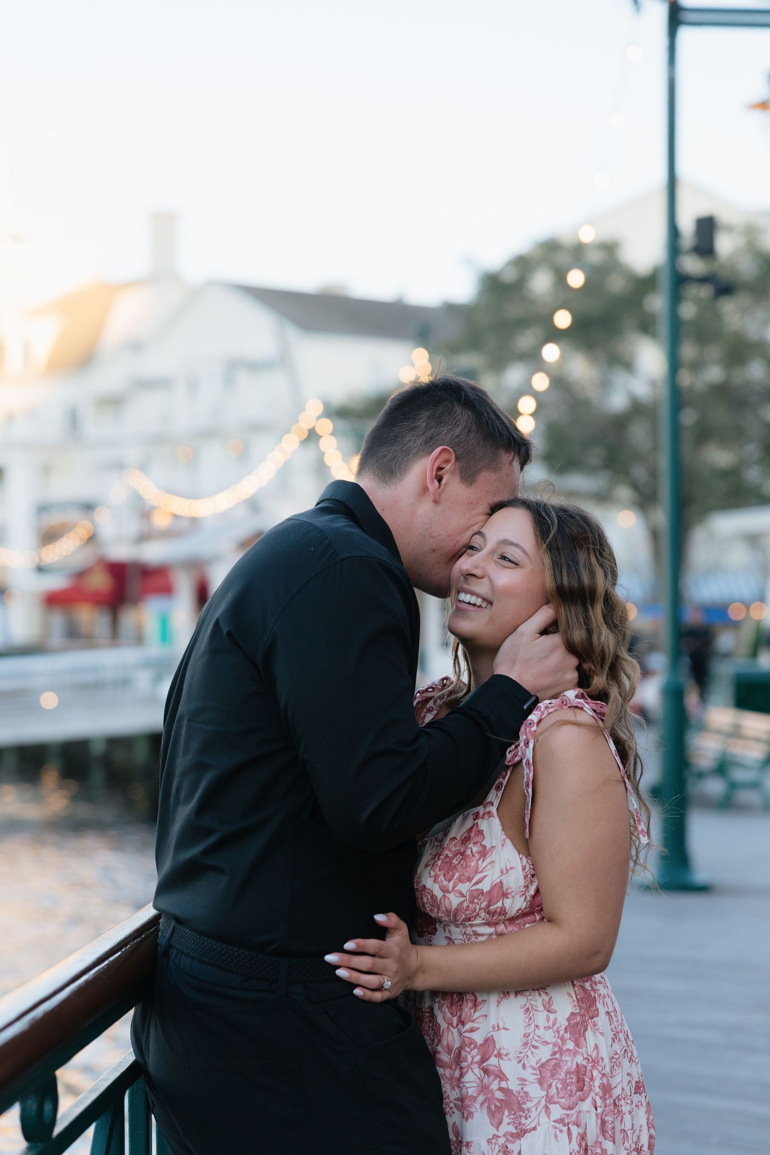 A romantic couple shares laughter and tender moments along a boardwalk during sunset.