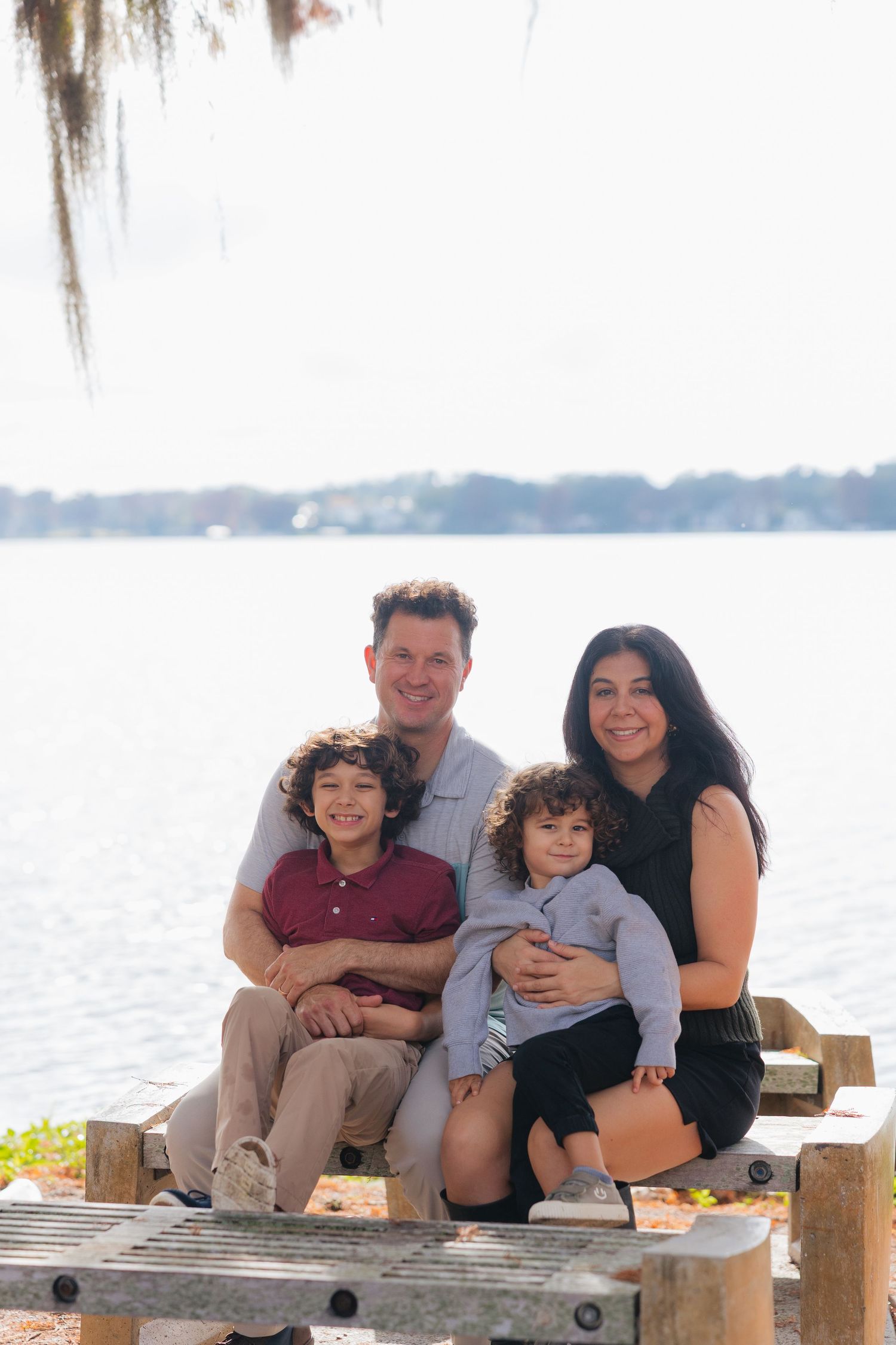 A family sits together on a wooden dock overlooking a serene lake on a bright day.