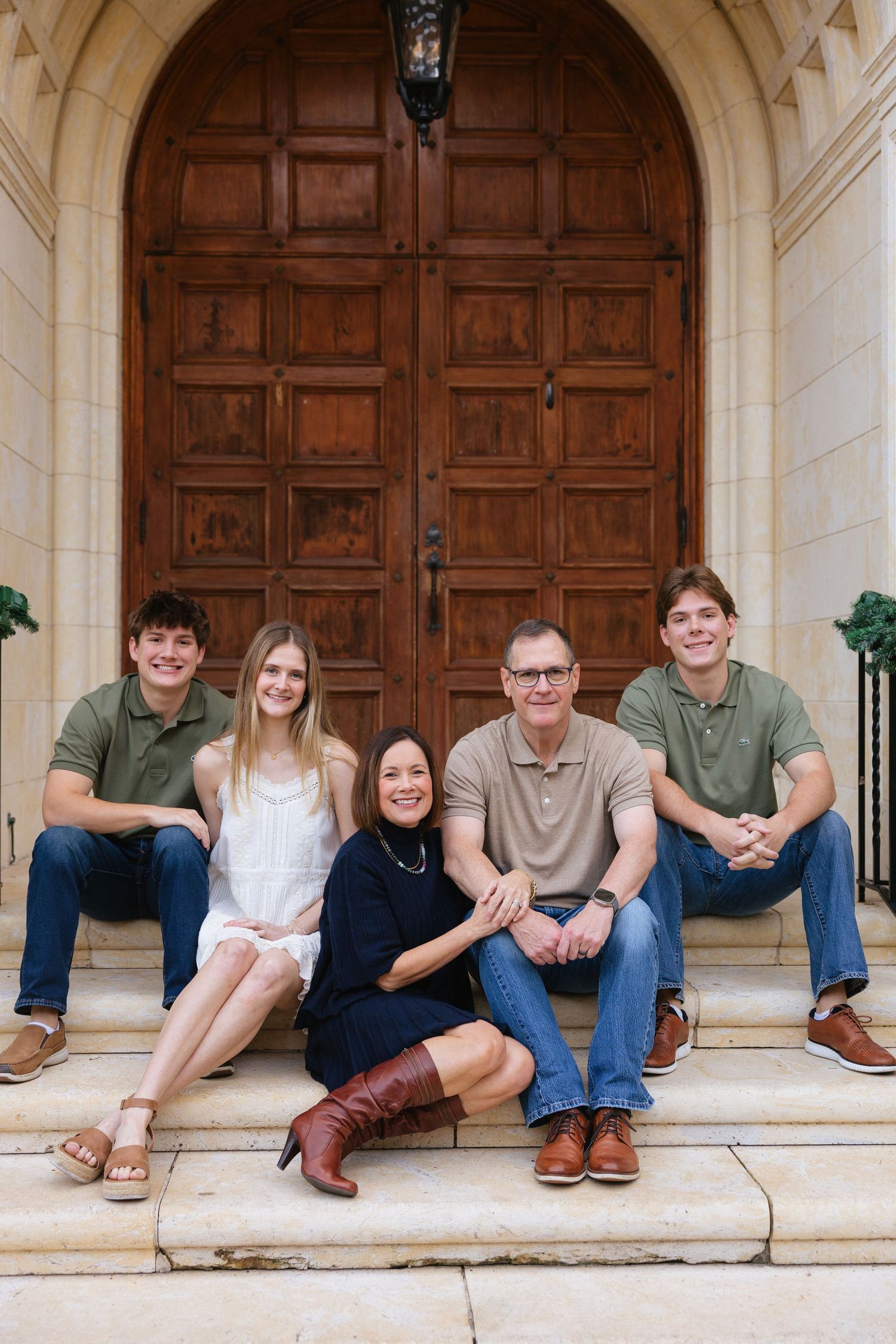 A group of people sitting casually on stone steps in front of wooden doors wearing casual clothing.