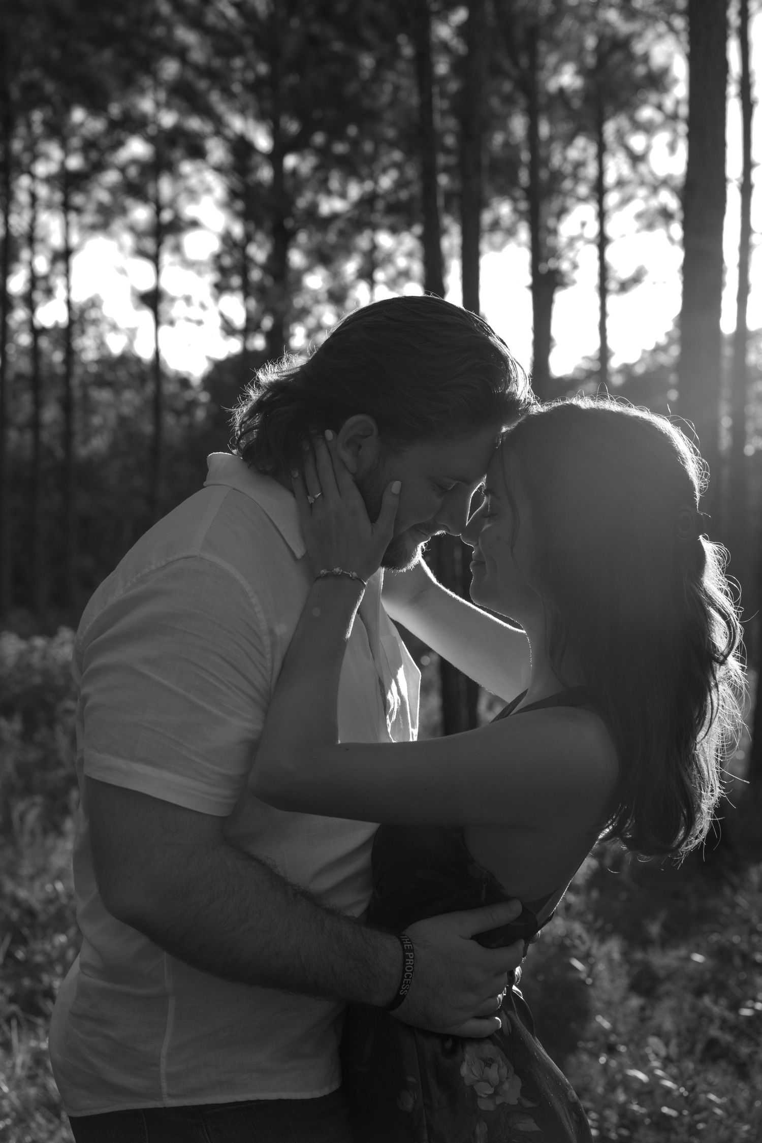 Silhouetted couple shares a tender moment against a wooded background in black and white.