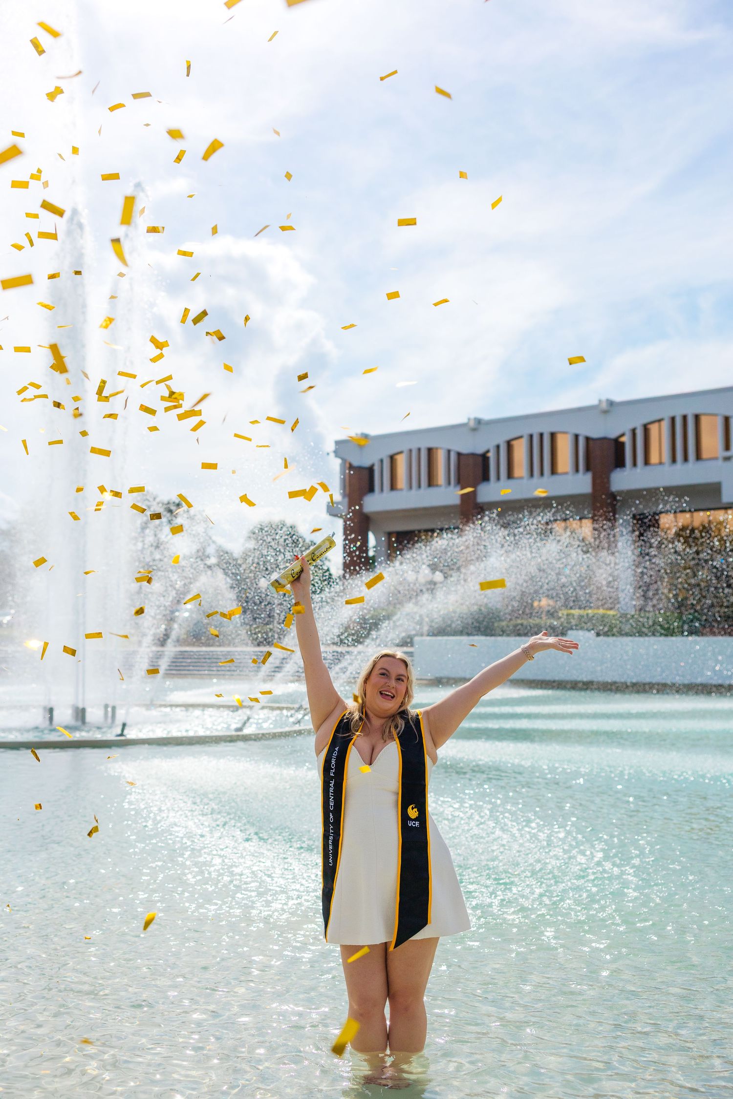 A person celebrates in a pool with confetti falling while wearing a black vest and holding a certificate.