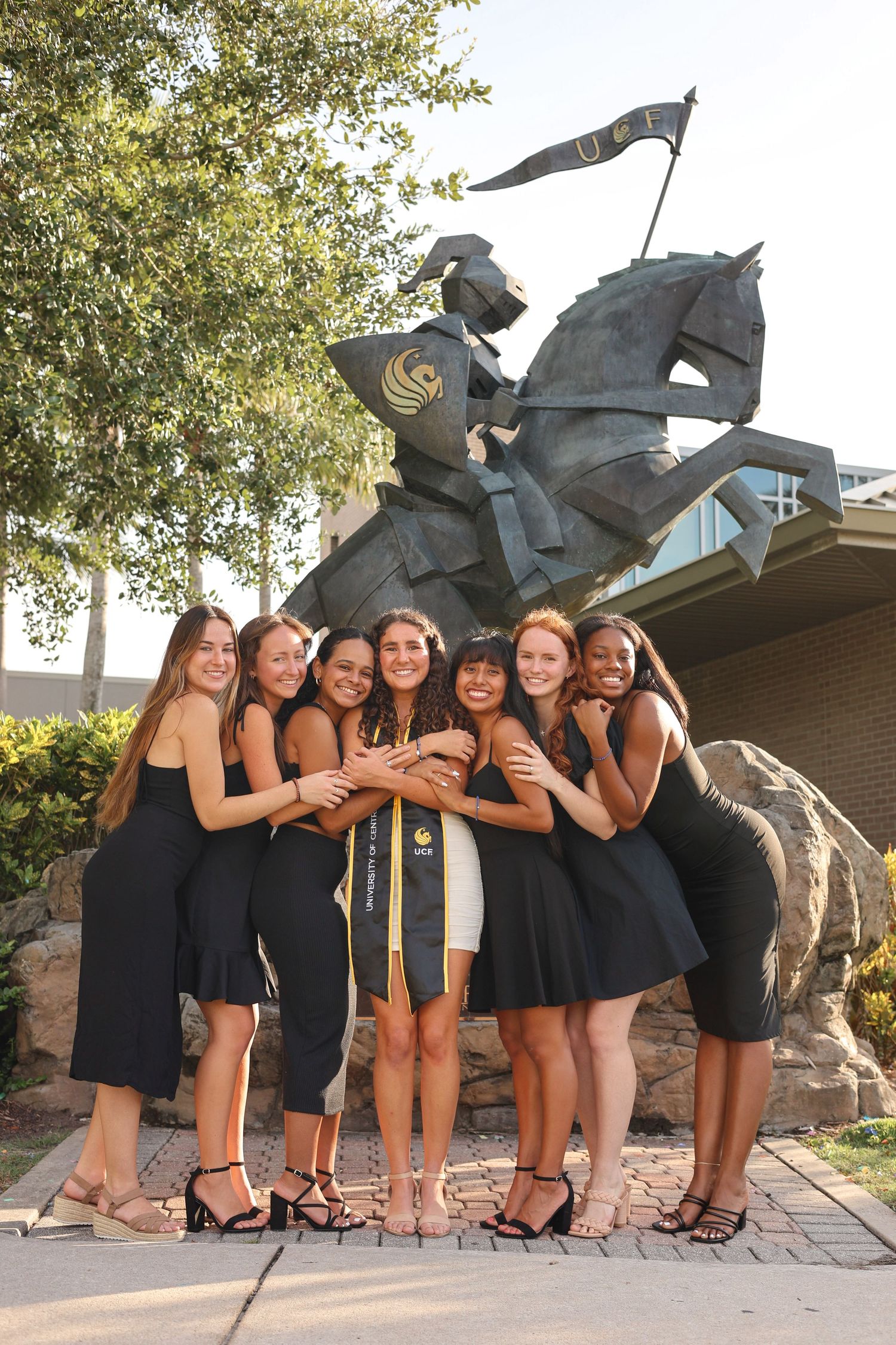 Group poses playfully in black dresses near a large outdoor sculpture.