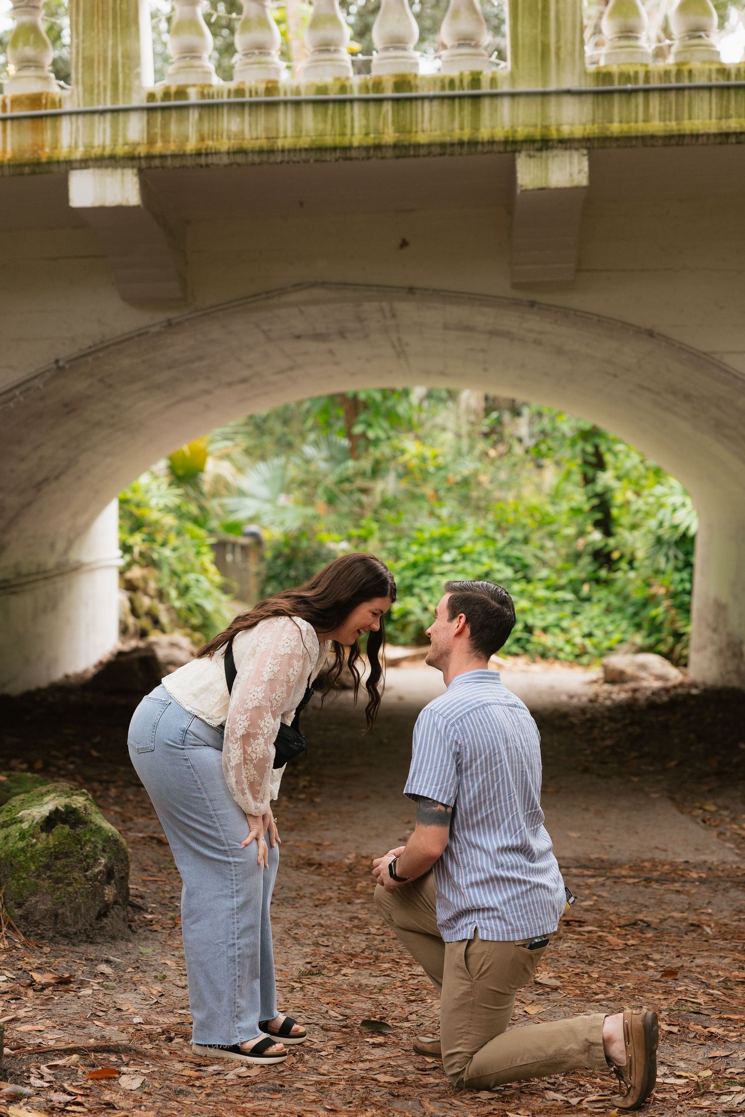 A couple shares a special moment under a stone bridge in a wooded area during a romantic photoshoot.