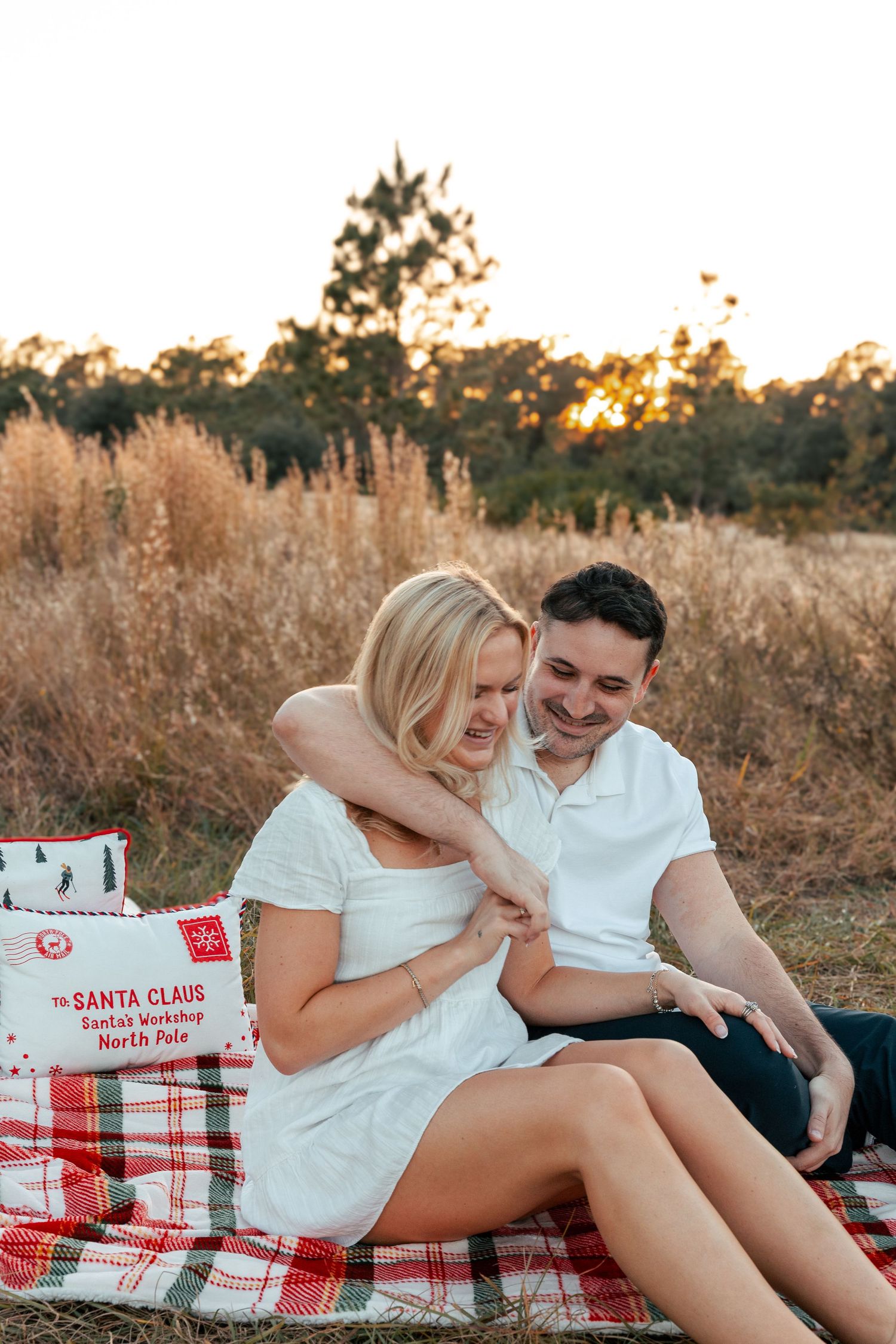 Couple sharing romantic moments on red plaid blanket during golden hour sunset in field of tall grass.