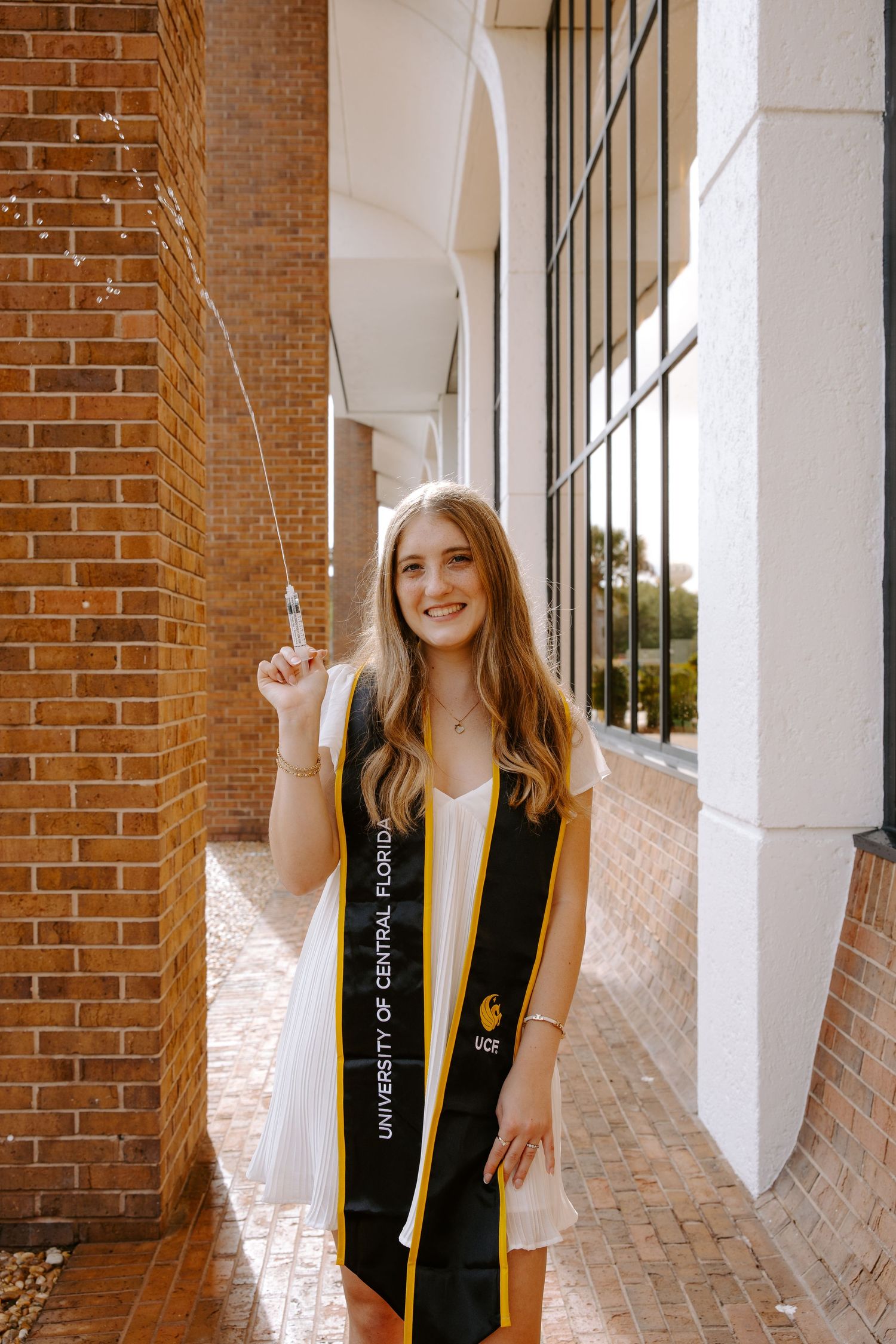 Graduate holding graduation tassel poses in archway with brick walls.