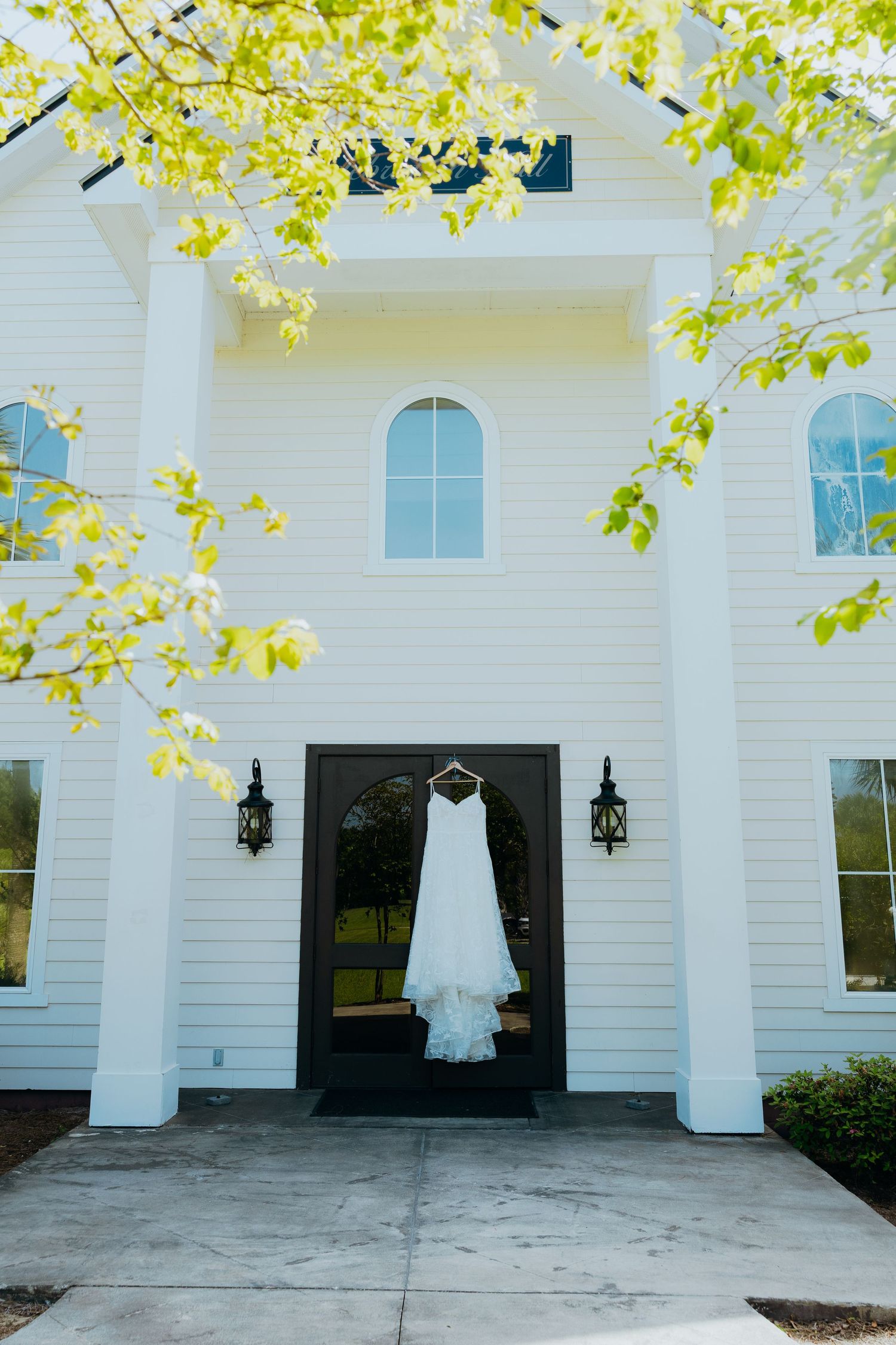 White wedding dress hanging outside classic white church building with arched windows.