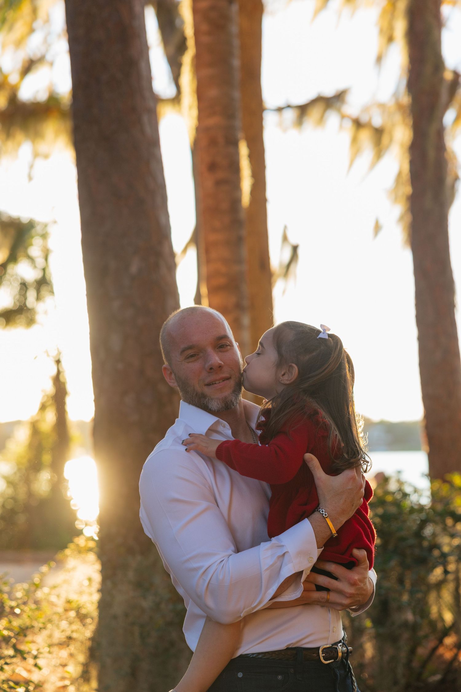 A couple shares a tender moment at sunset in a palm tree grove, with golden sunlight filtering through the trees.