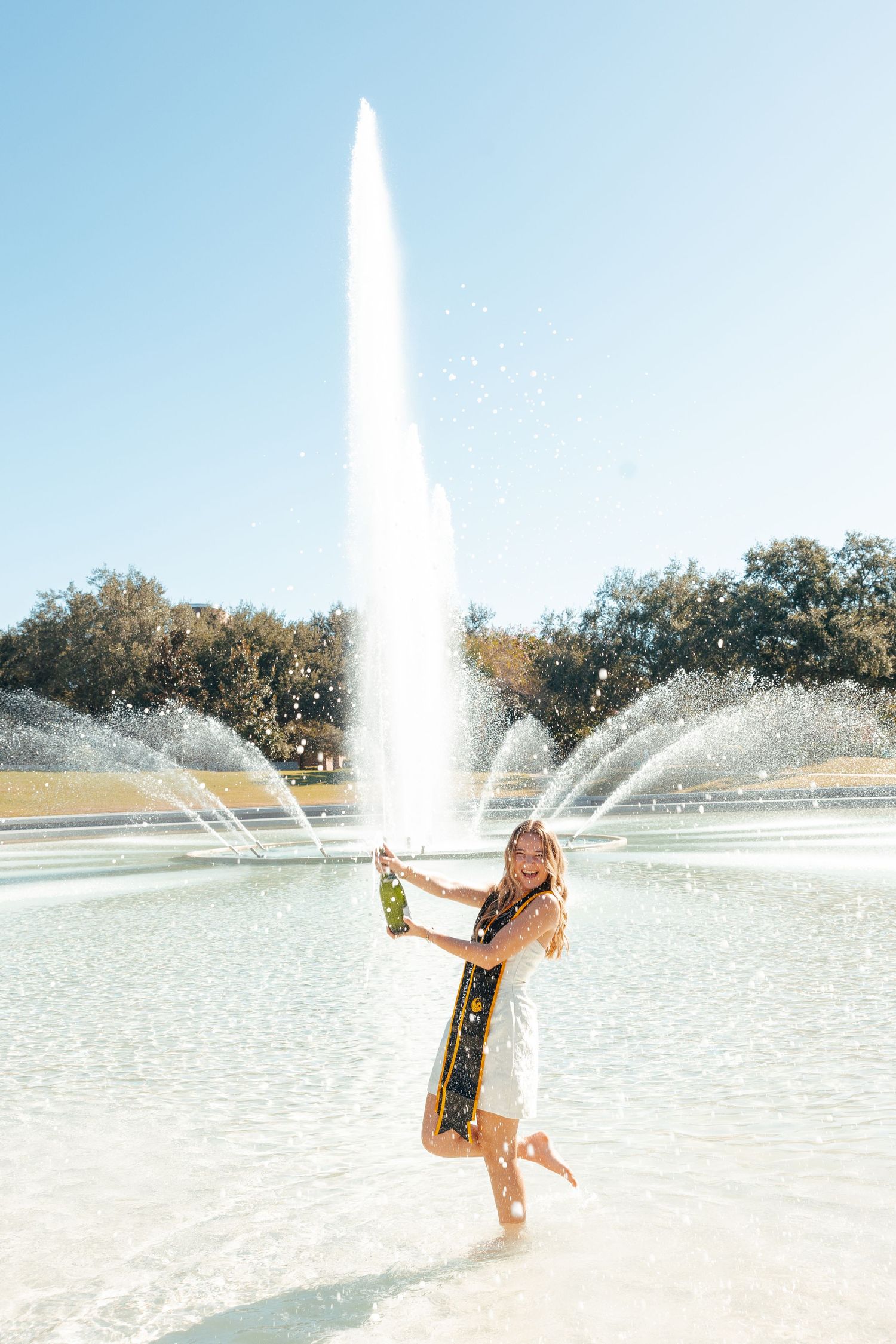 A sequence of four photos shows someone joyfully posing and dancing in front of a large fountain on a sunny day.