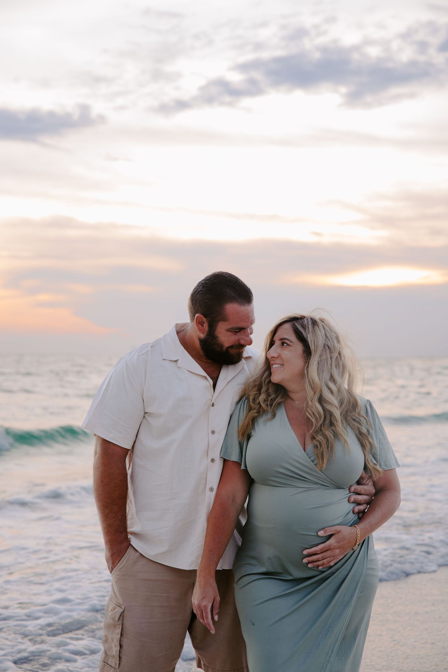 Expecting couple sharing intimate moments during sunset beach photoshoot.