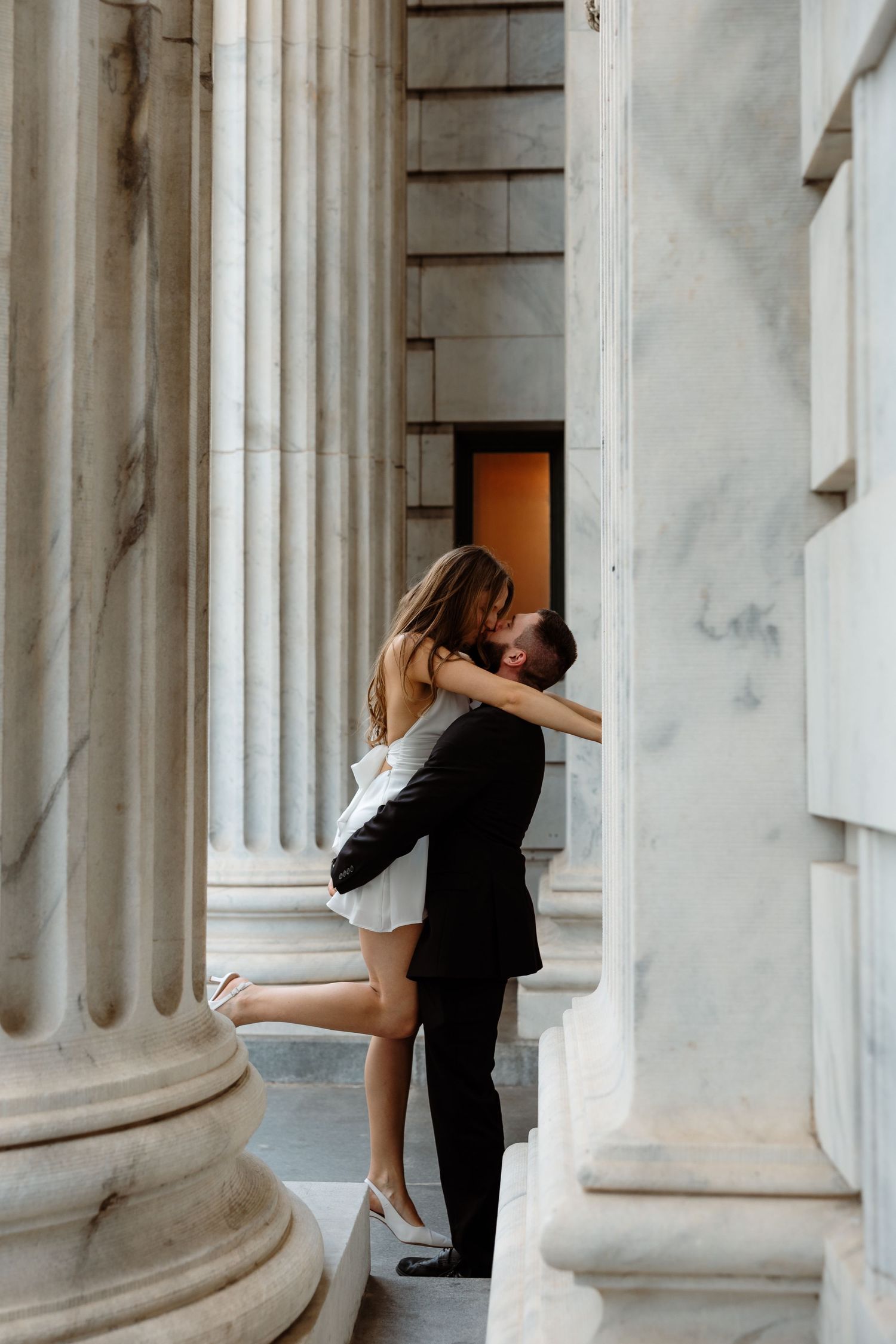 Affectionate couple shares intimate moment between white marble pillars.
