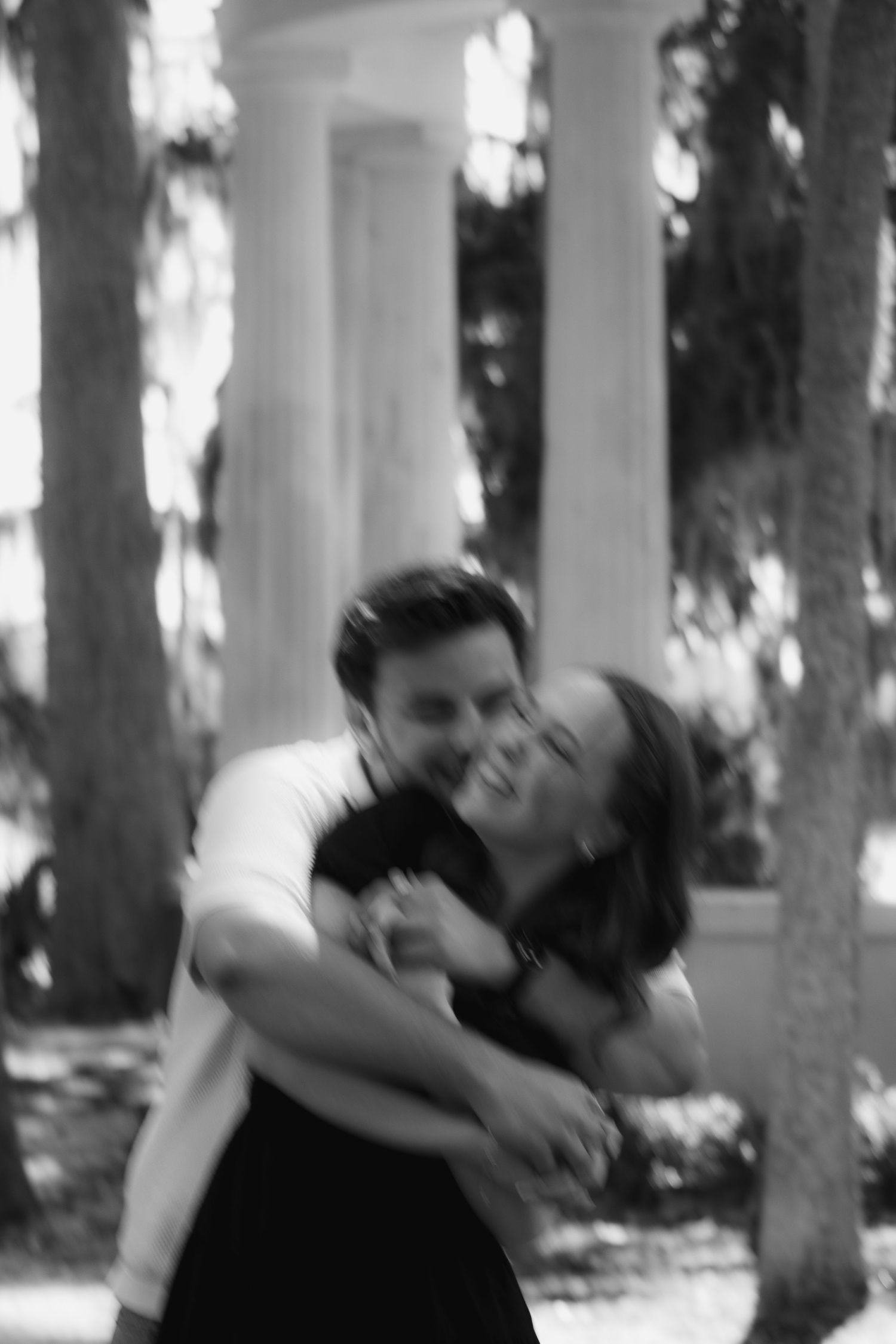 A black and white candid photo of a joyful couple embracing and laughing together outdoors.