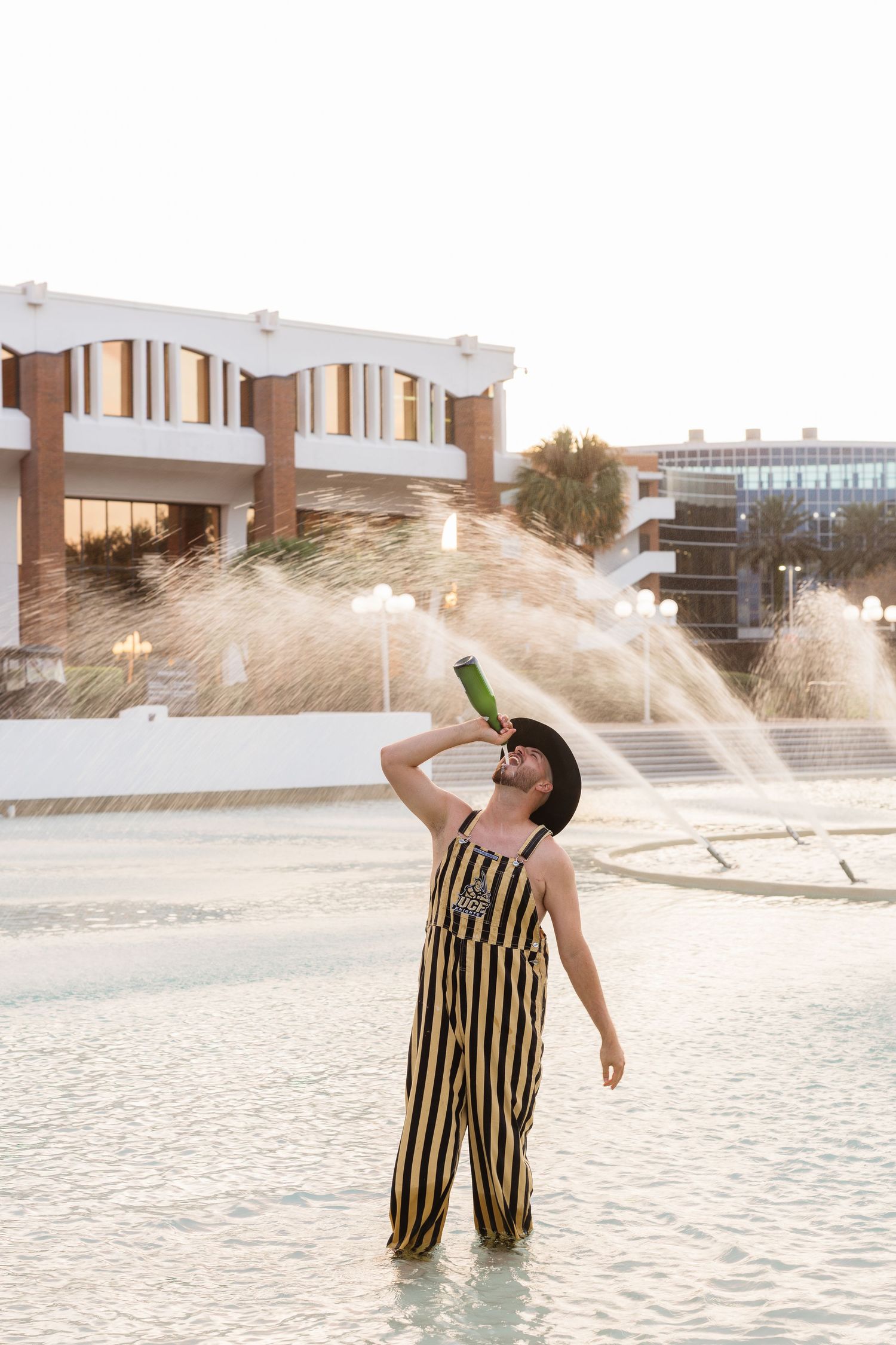 Person in black and gold striped outfit splashing in shallow water during golden hour sunset.