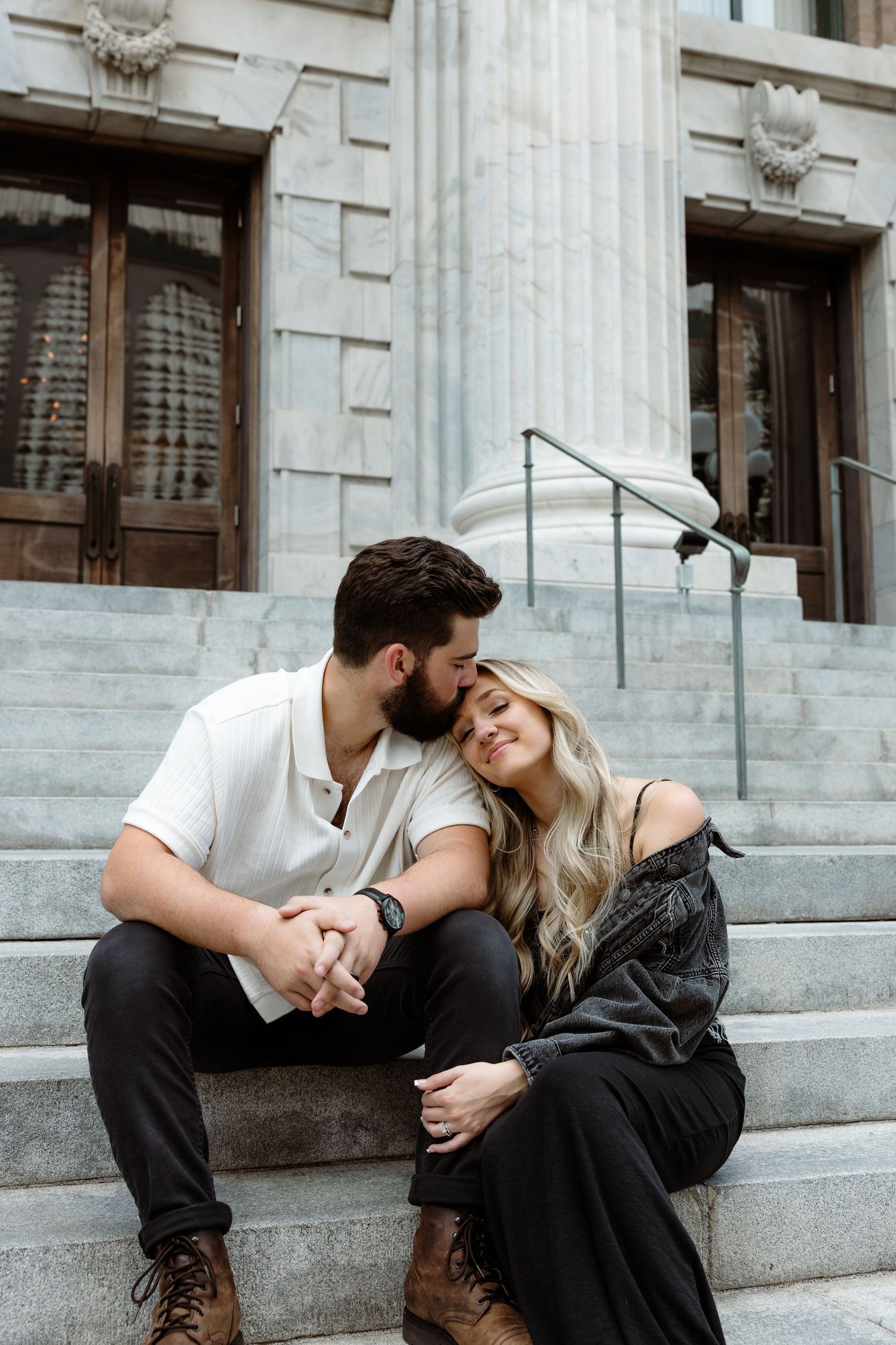Romantic couple sharing intimate moments on stone steps of historic building with white columns.