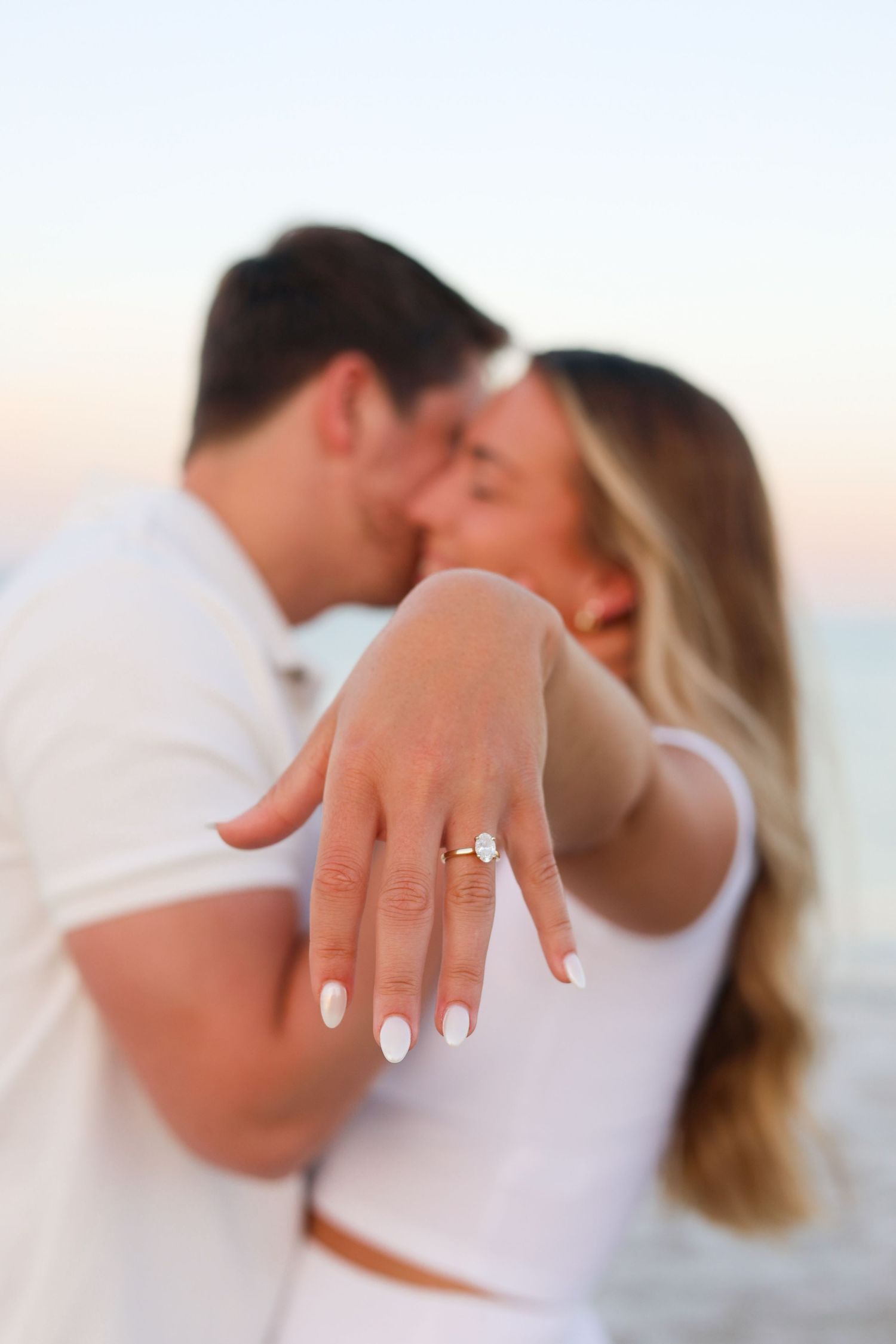 Close-up of engagement ring on woman's hand during romantic beach photoshoot.