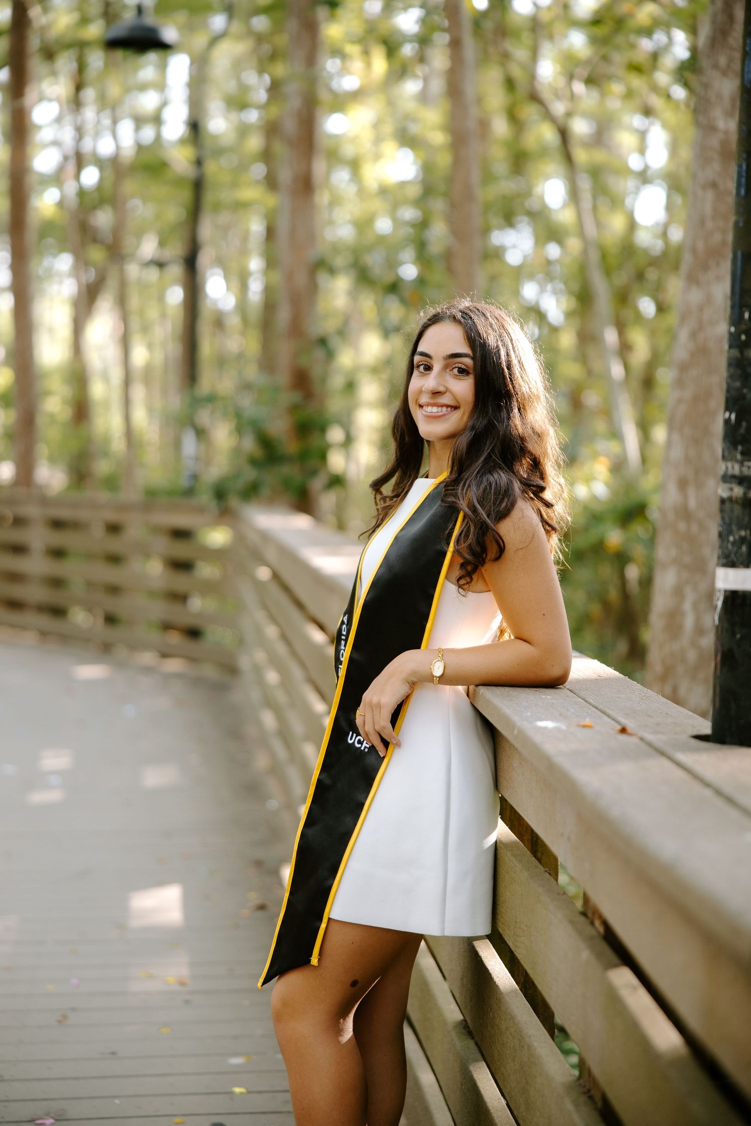 Graduate photos taken on wooden boardwalk surrounded by trees.
