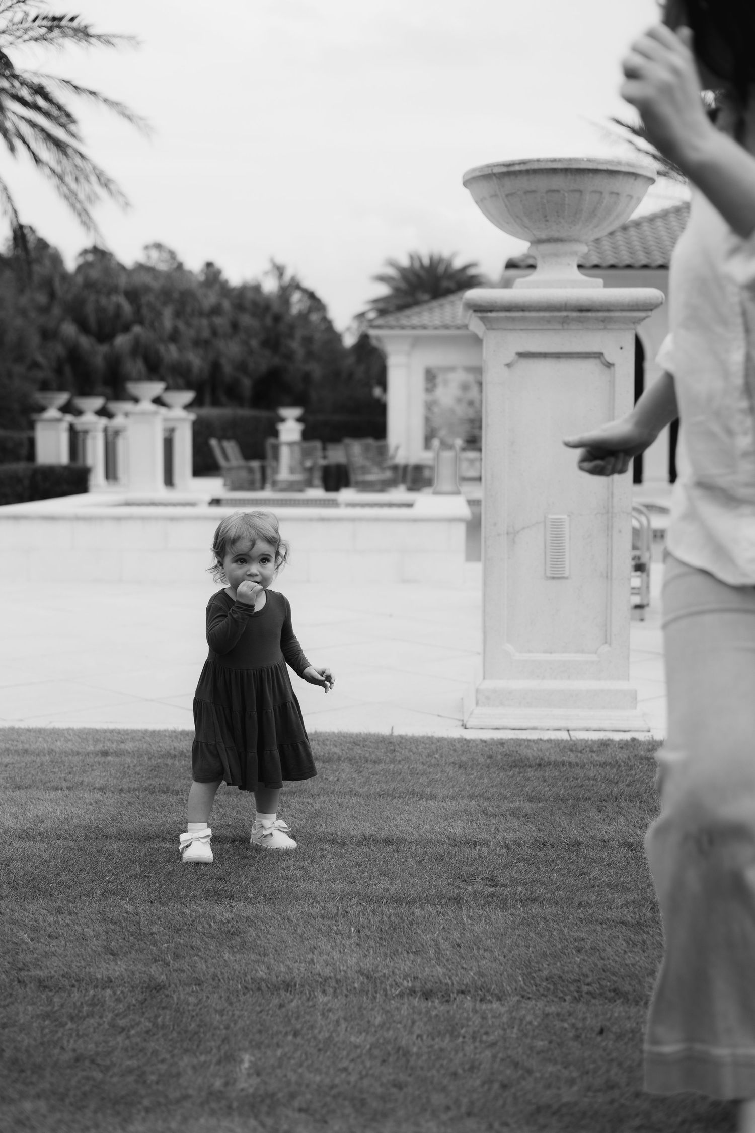 Black and white photo series of a small child playing on a grassy lawn near white architectural columns.