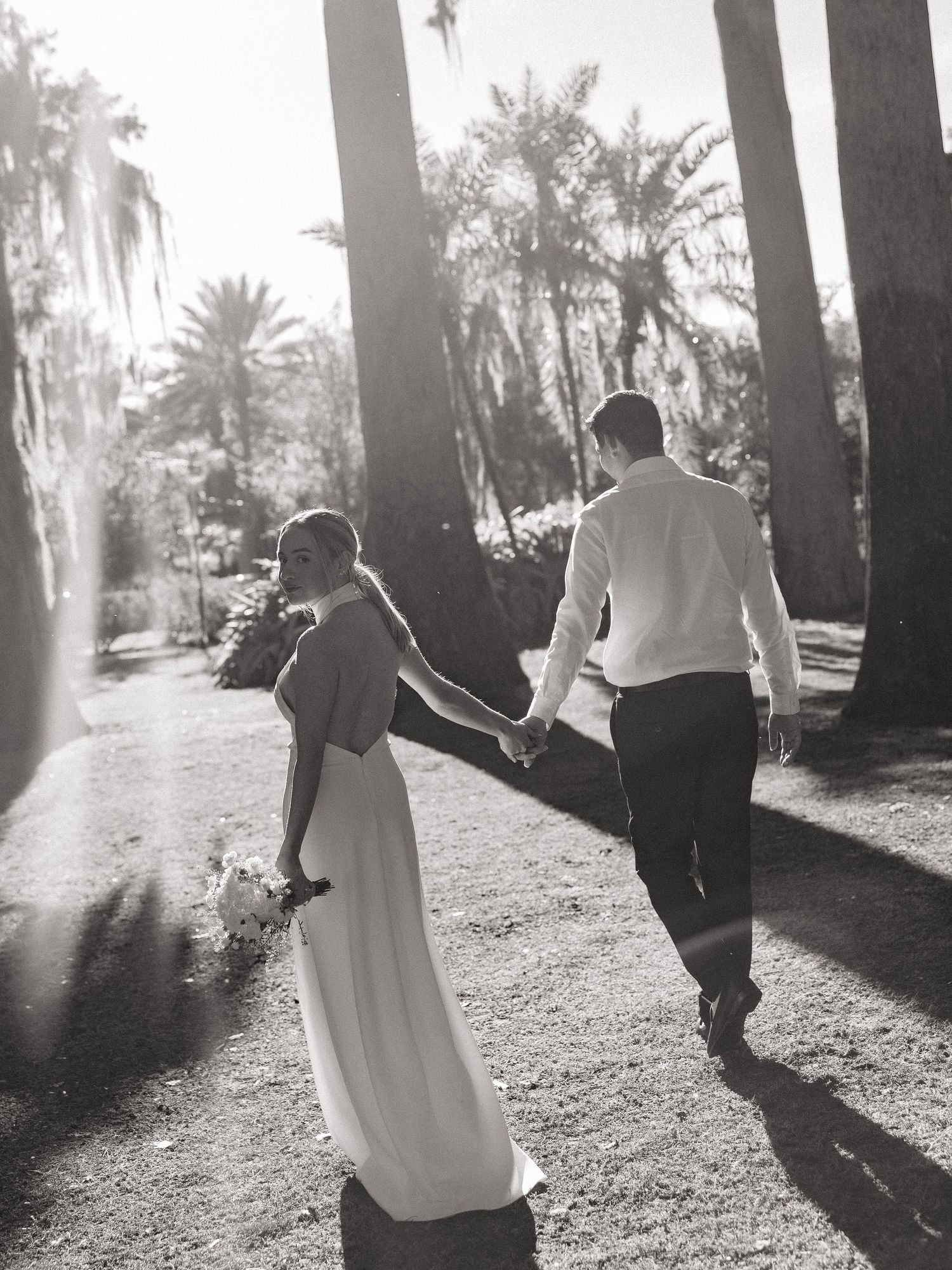 Couple dancing and twirling in a dreamy sunlit outdoor setting with tall palm trees creating dramatic shadows.