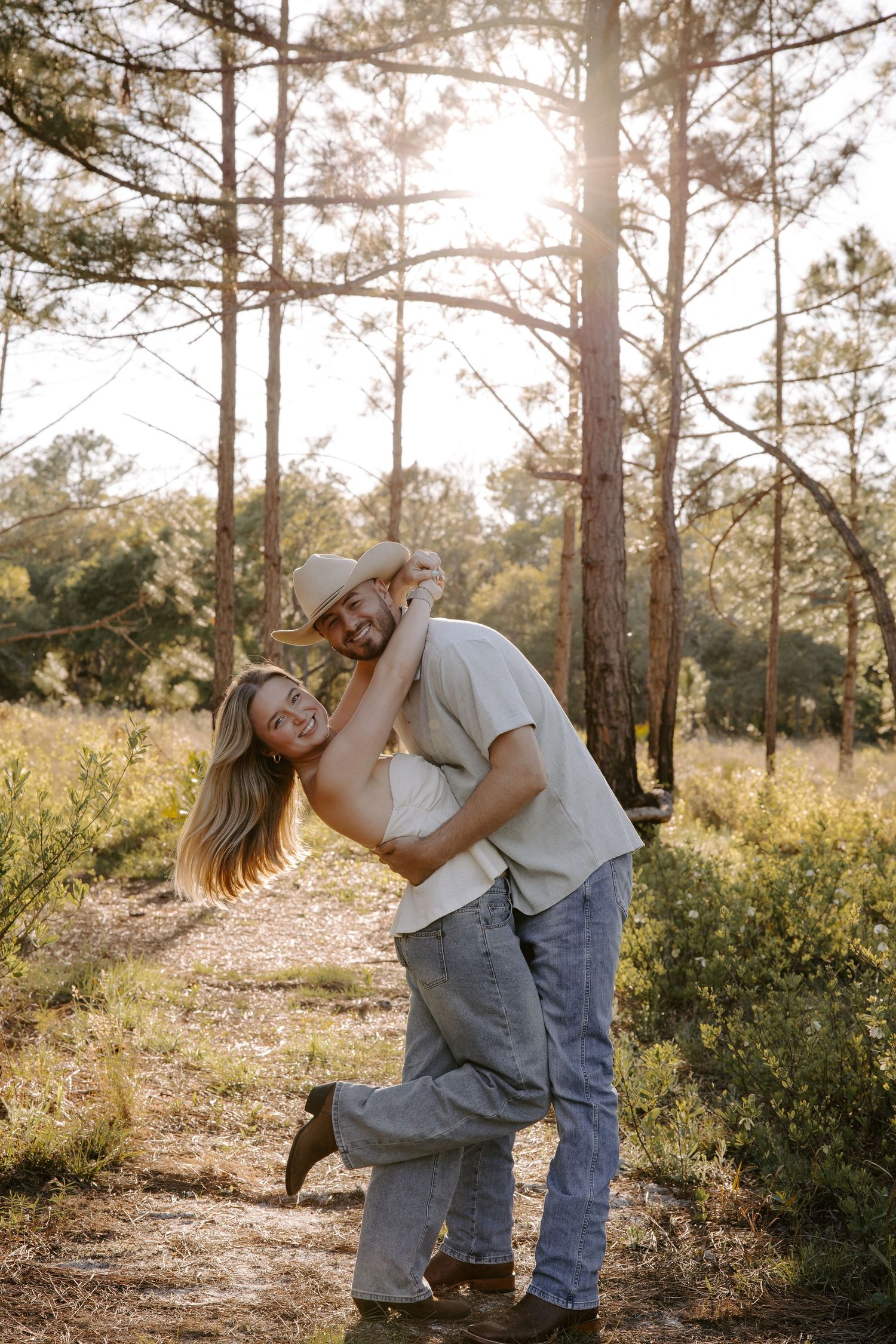 A couple shares a romantic moment while dancing together on a sunlit forest path during golden hour.