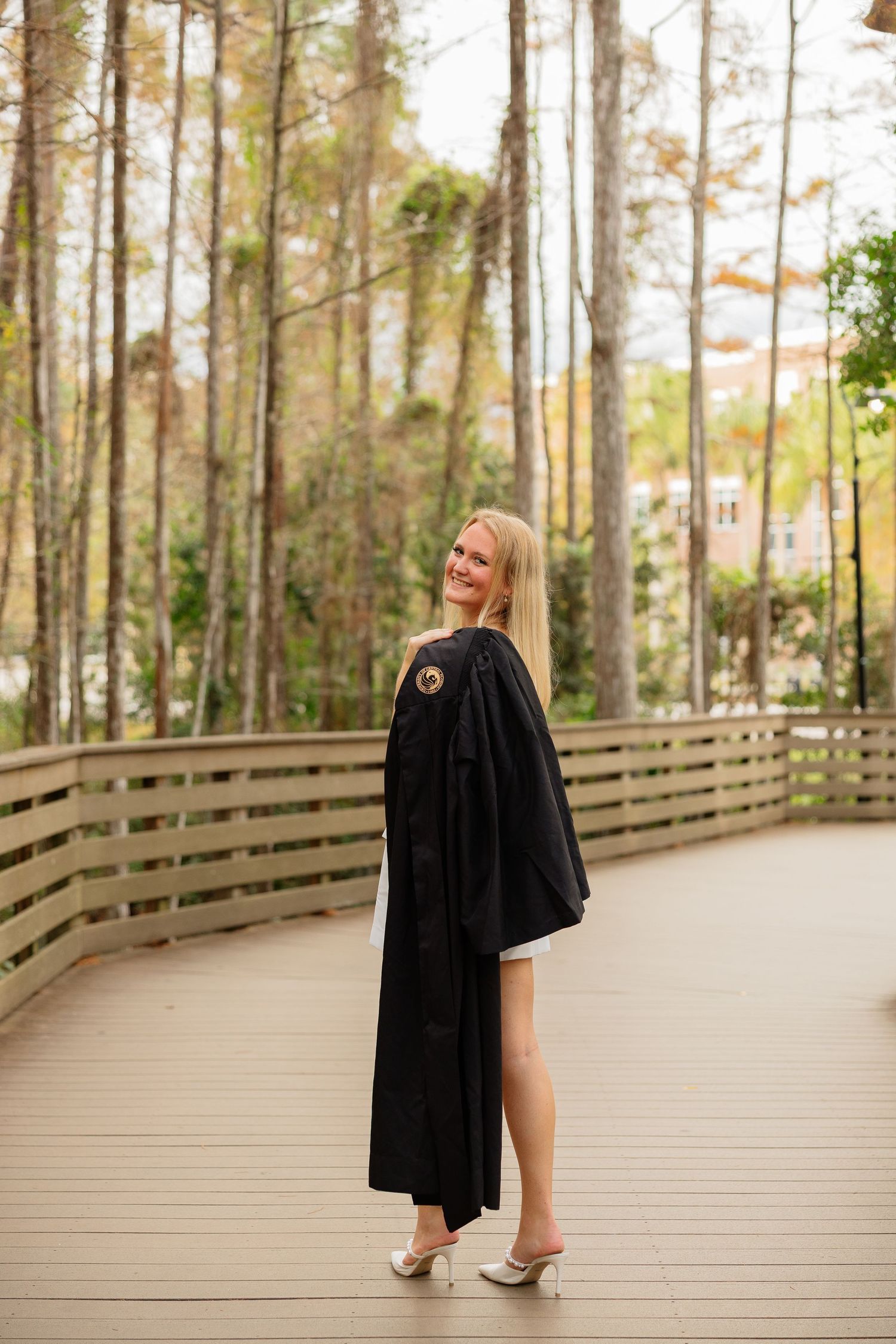 A series of photos showing someone in a graduation gown walking along a wooden boardwalk surrounded by tall pine trees.