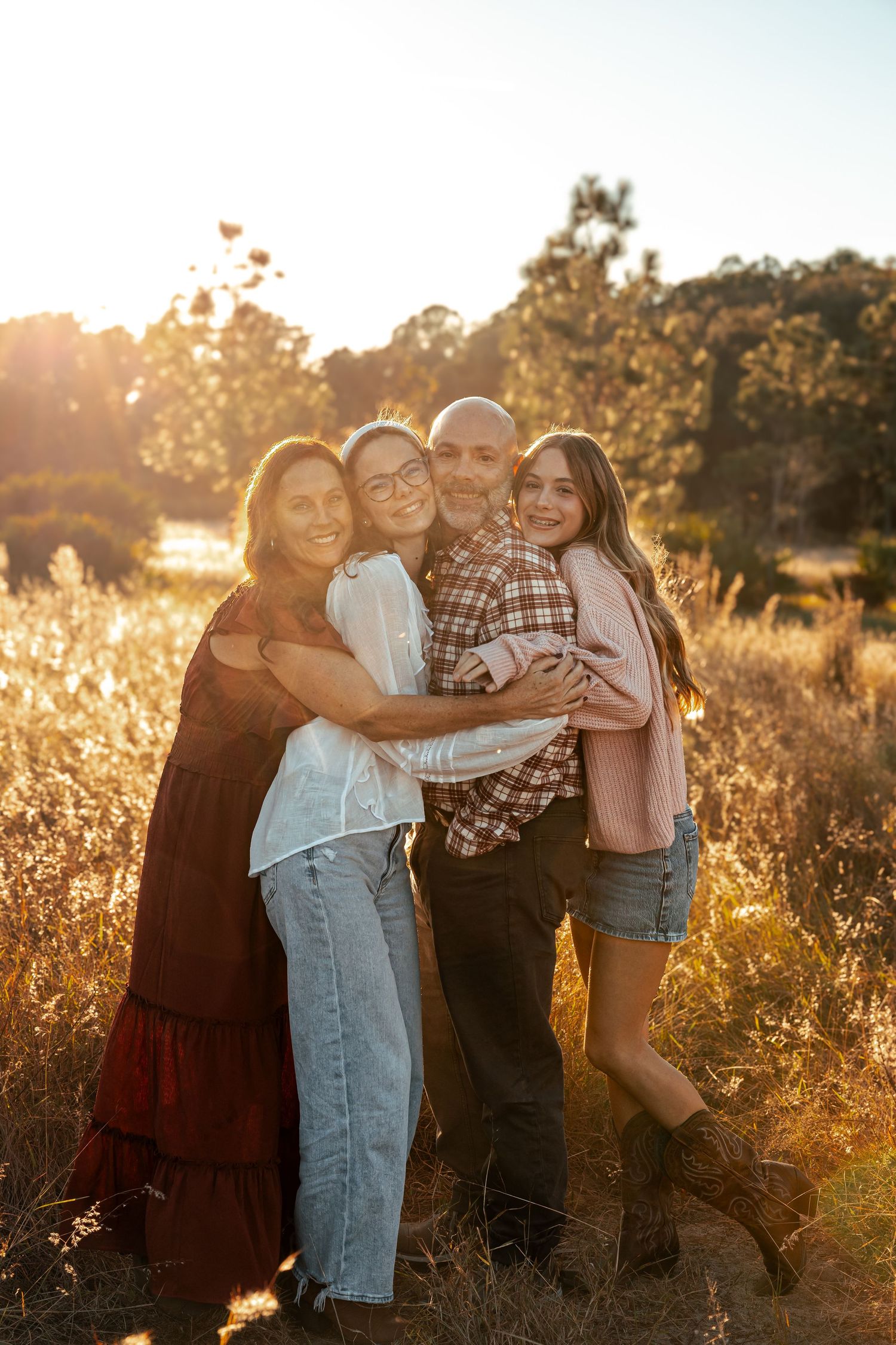 A family shares joyful embraces in a golden sunlit field during sunset.