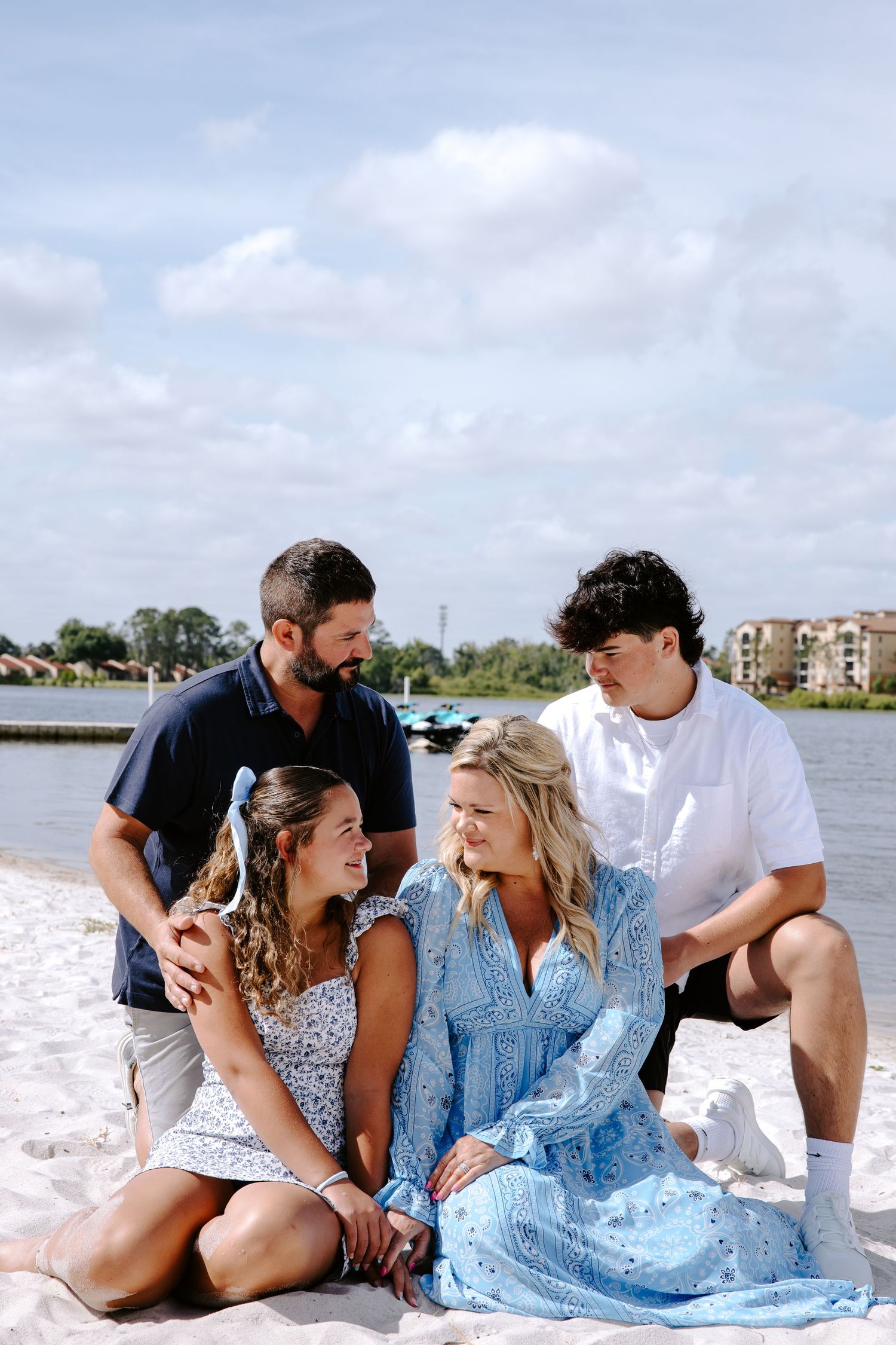 Family enjoying a sunny day at the beach with casual poses on white sand.