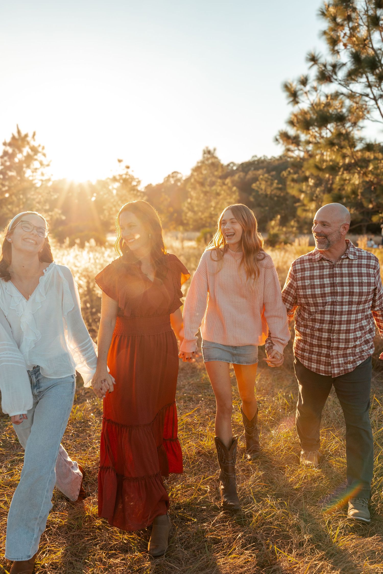 A large group stands together in a line at sunset with golden sunlight streaming through pine trees behind them.