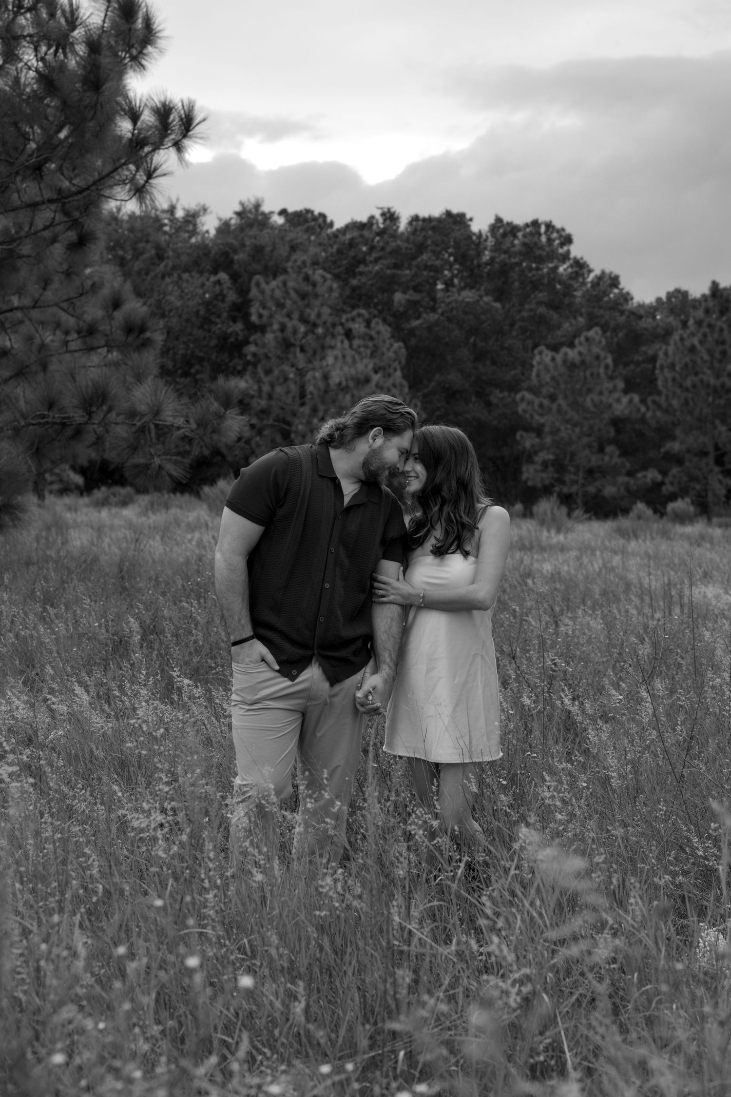 A couple embracing in a wildflower meadow with trees in the background, captured in black and white.
