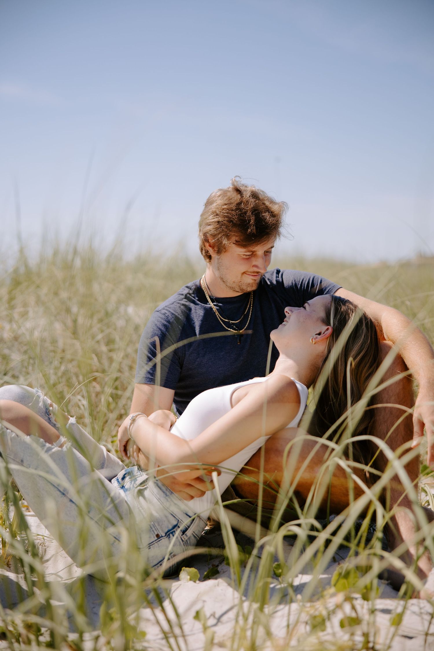 Young couple lounging together in tall grass on a sunny day.
