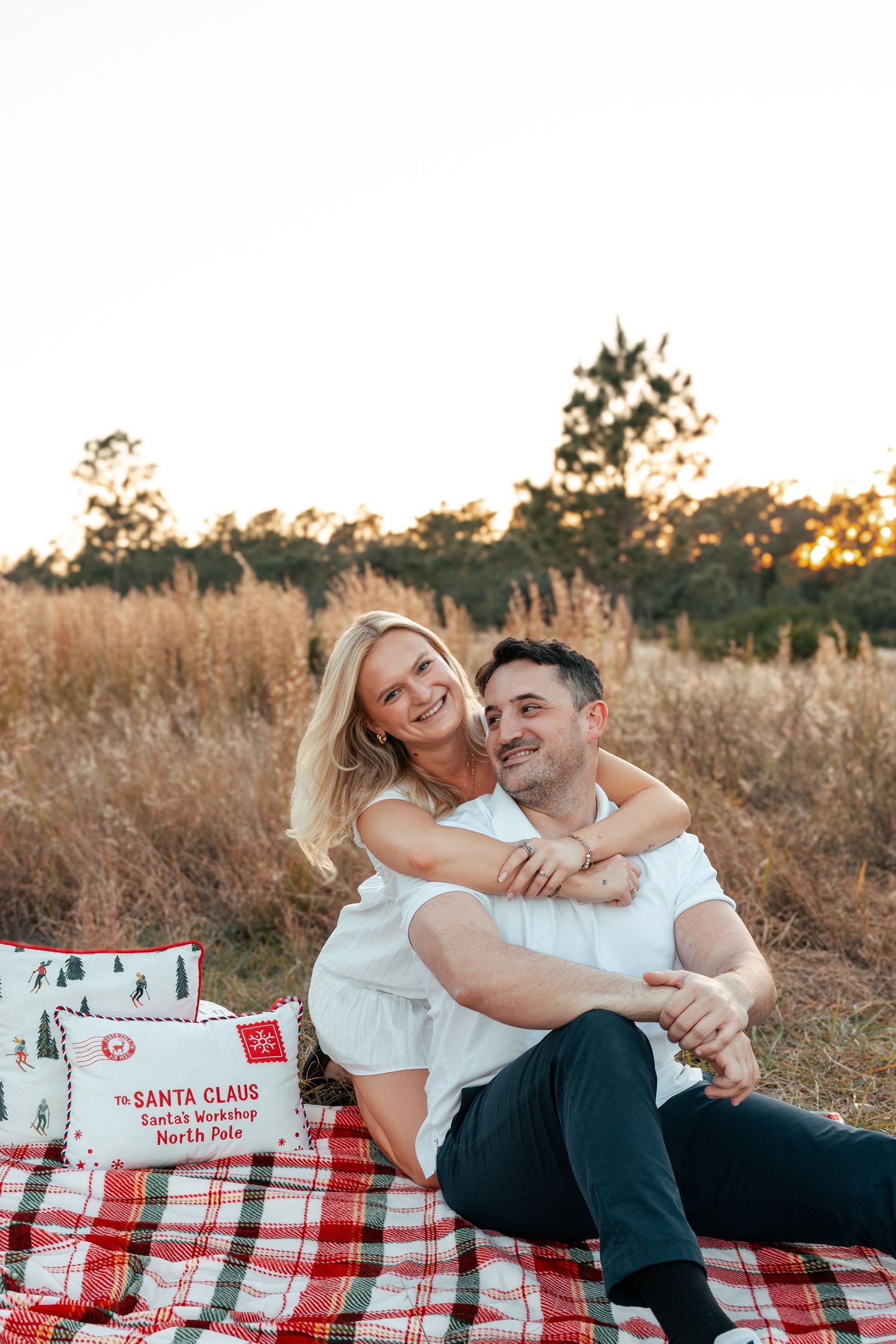 Couple relaxing on red plaid blanket in golden field during sunset photoshoot.