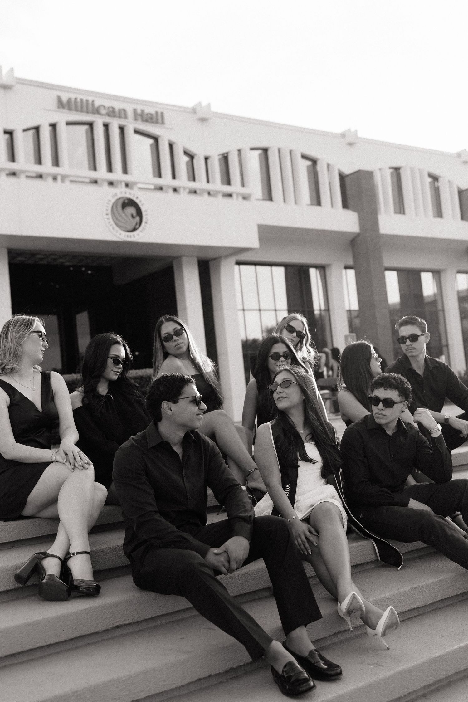 Black and white photo of stylish group sitting on steps outside Millican Hall building.