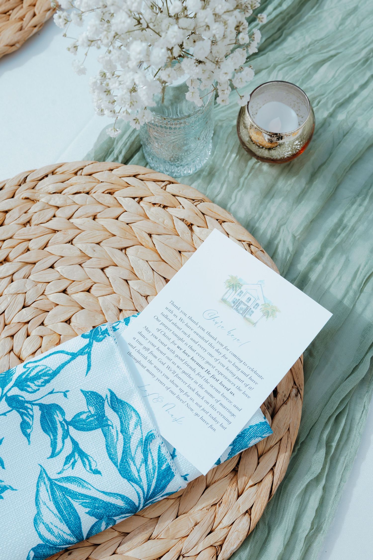 Wedding invitation details on woven placemat with blue floral design and glassware.