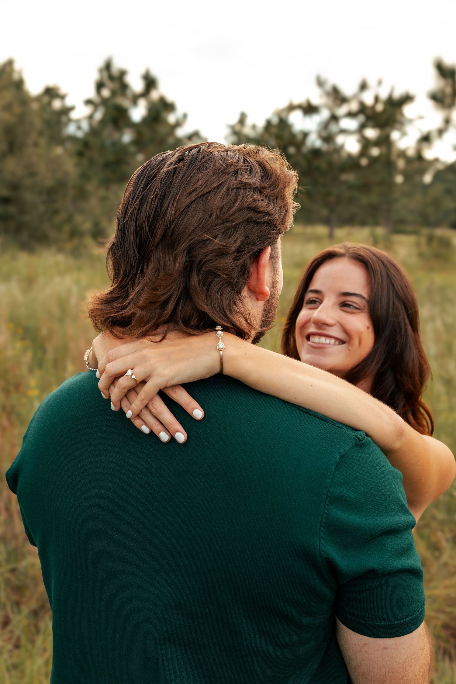 A couple embrace warmly in a field at sunset, her arm wrapped around his green sweater in four progressive shots.