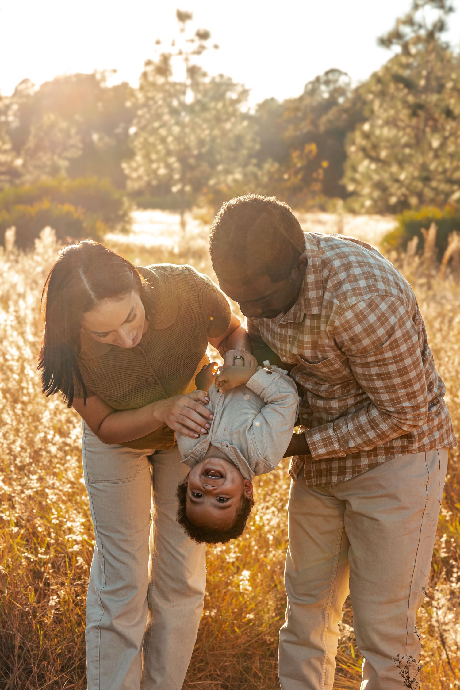 A loving family shares playful moments in a golden sunlit field during sunset.