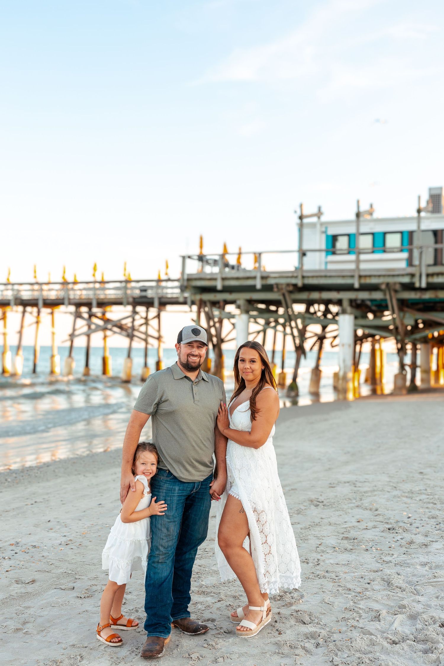 Family enjoying a sunset beach photoshoot along a wooden pier in casual summer attire.
