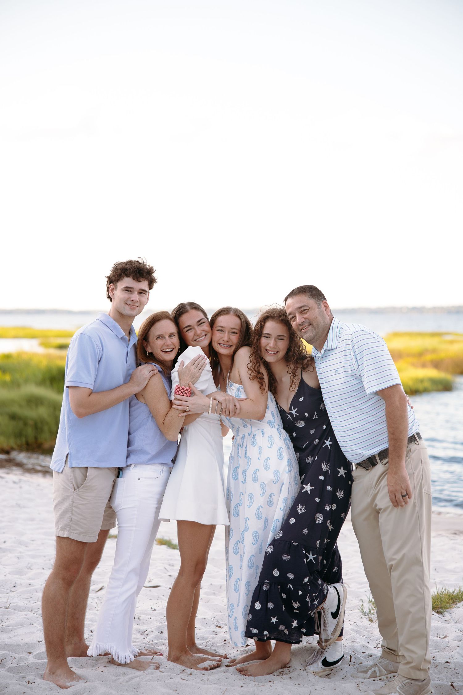 Group wearing white and blue outfits poses together on beach at sunset.