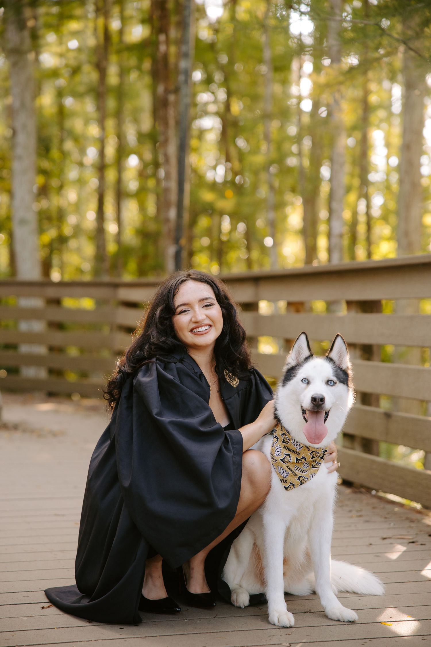 Husky dog wearing a bandana poses with companion on wooden deck in forest setting.