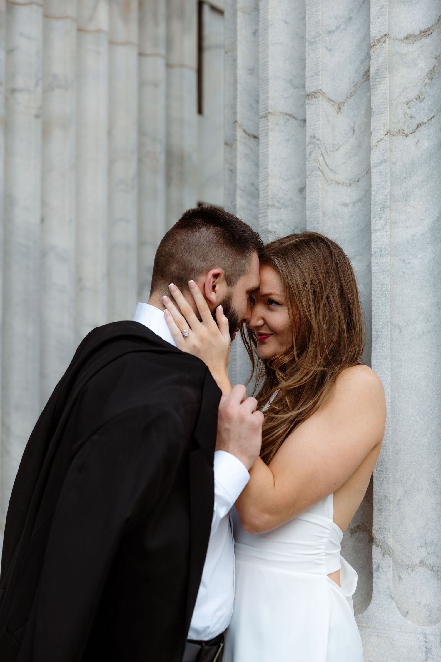 Romantic wedding couple shares an intimate moment against white marble columns.
