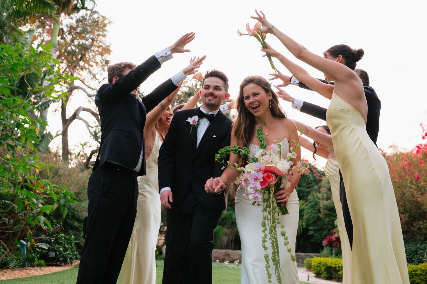A wedding party celebrates joyfully outdoors with raised arms and laughter during an autumn ceremony.
