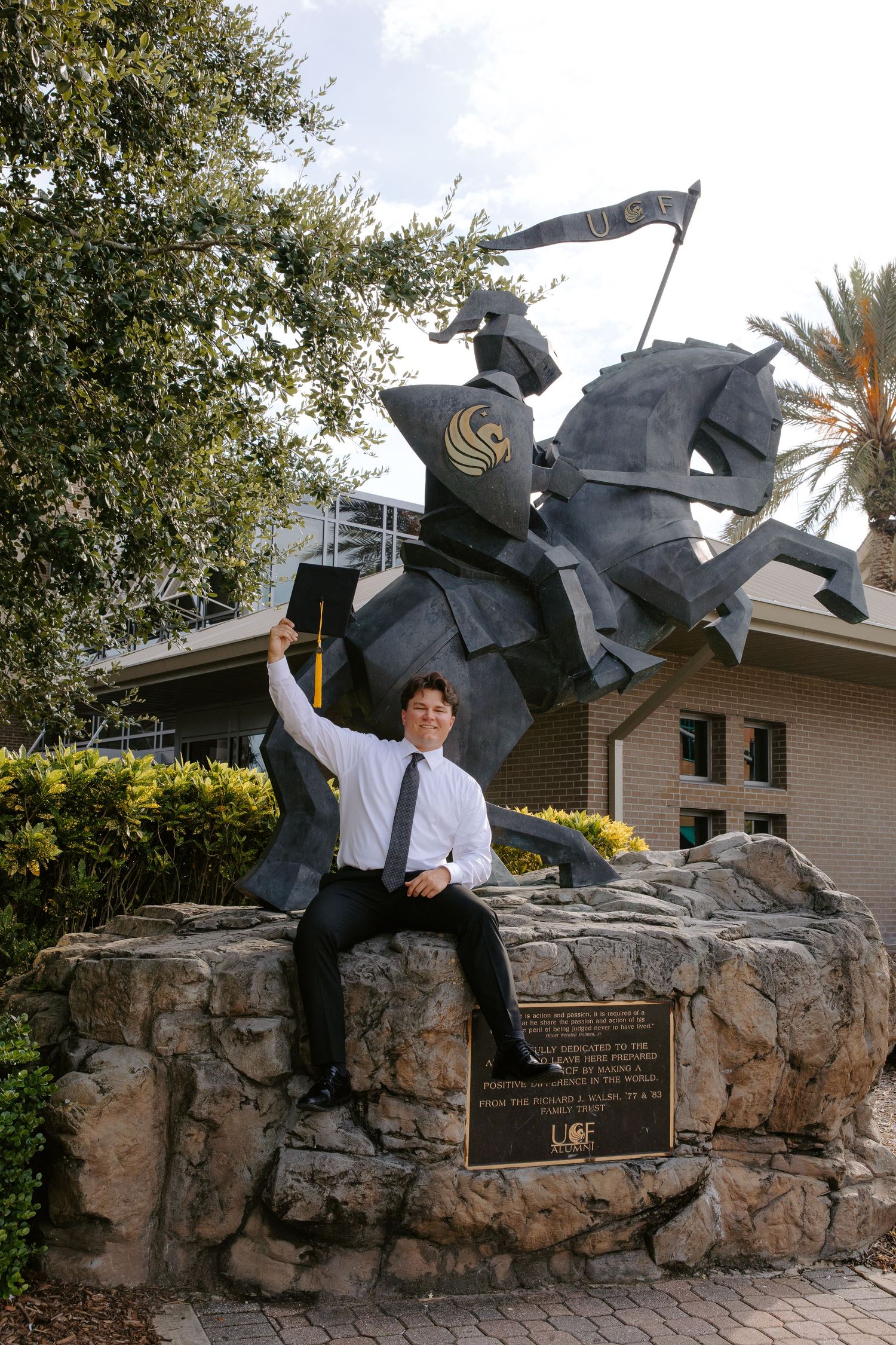 Graduate poses with UCF knight statue on campus grounds.