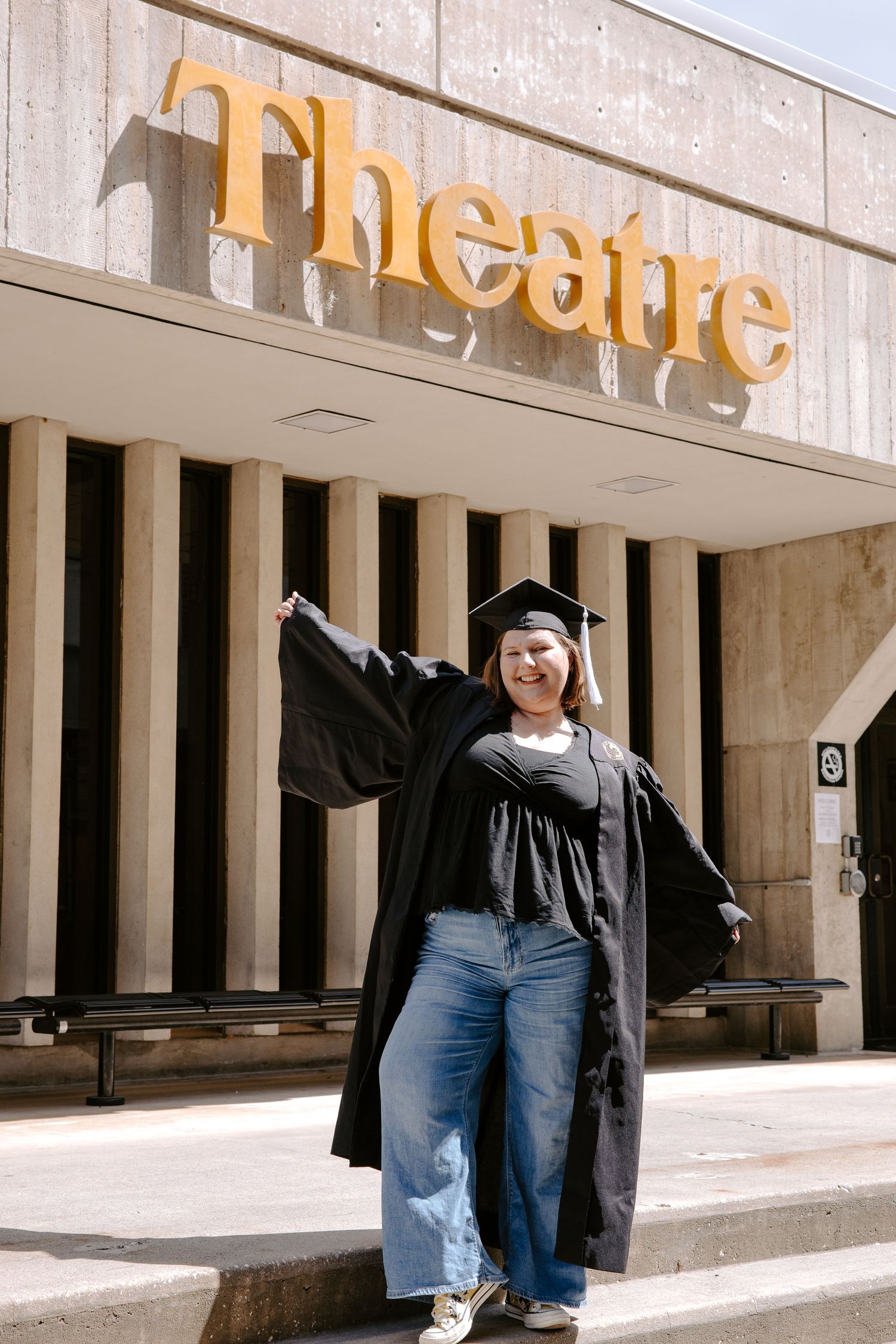Graduate poses in front of theatre building columns during graduation photoshoot.