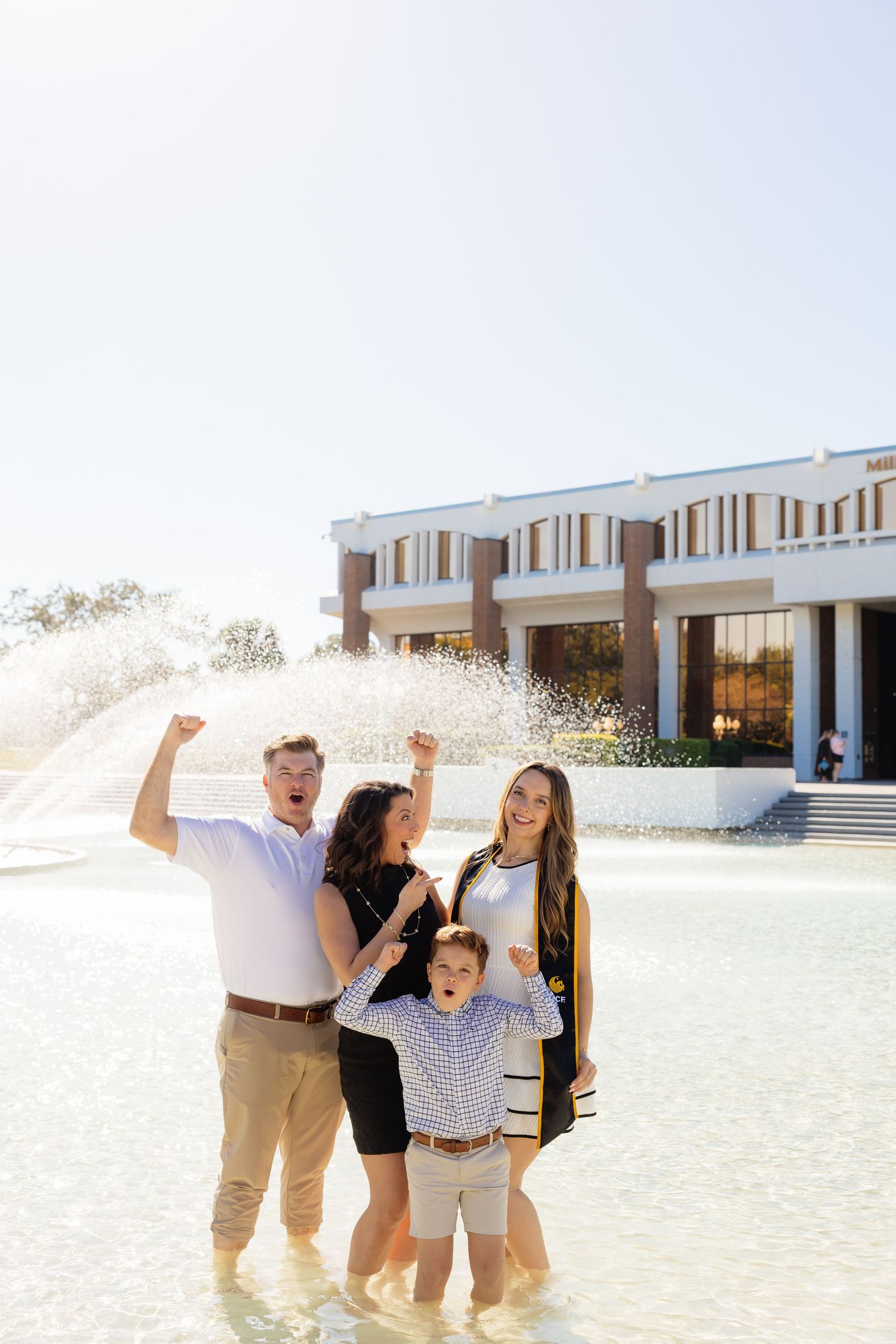 A joyful family celebrates together in front of a modern building on a bright sunny day.
